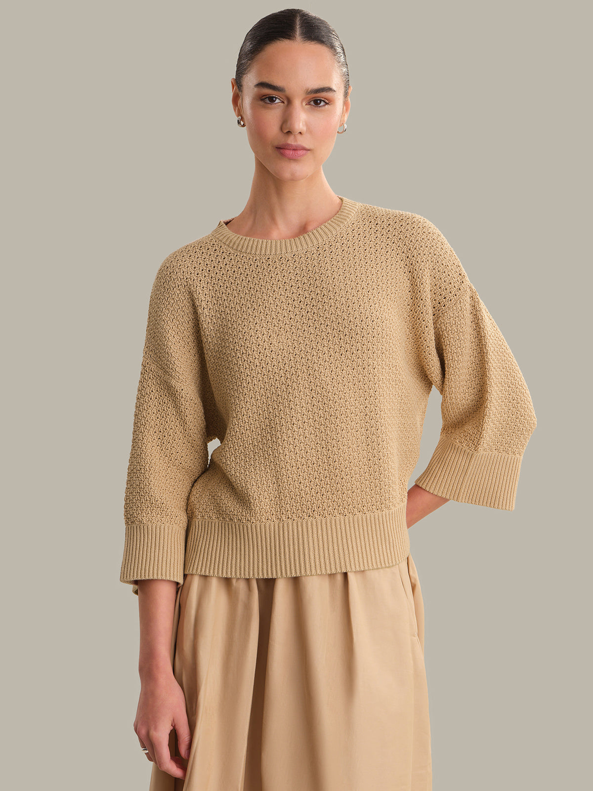 Woman wearing a beige sweater and skirt against a neutral background
