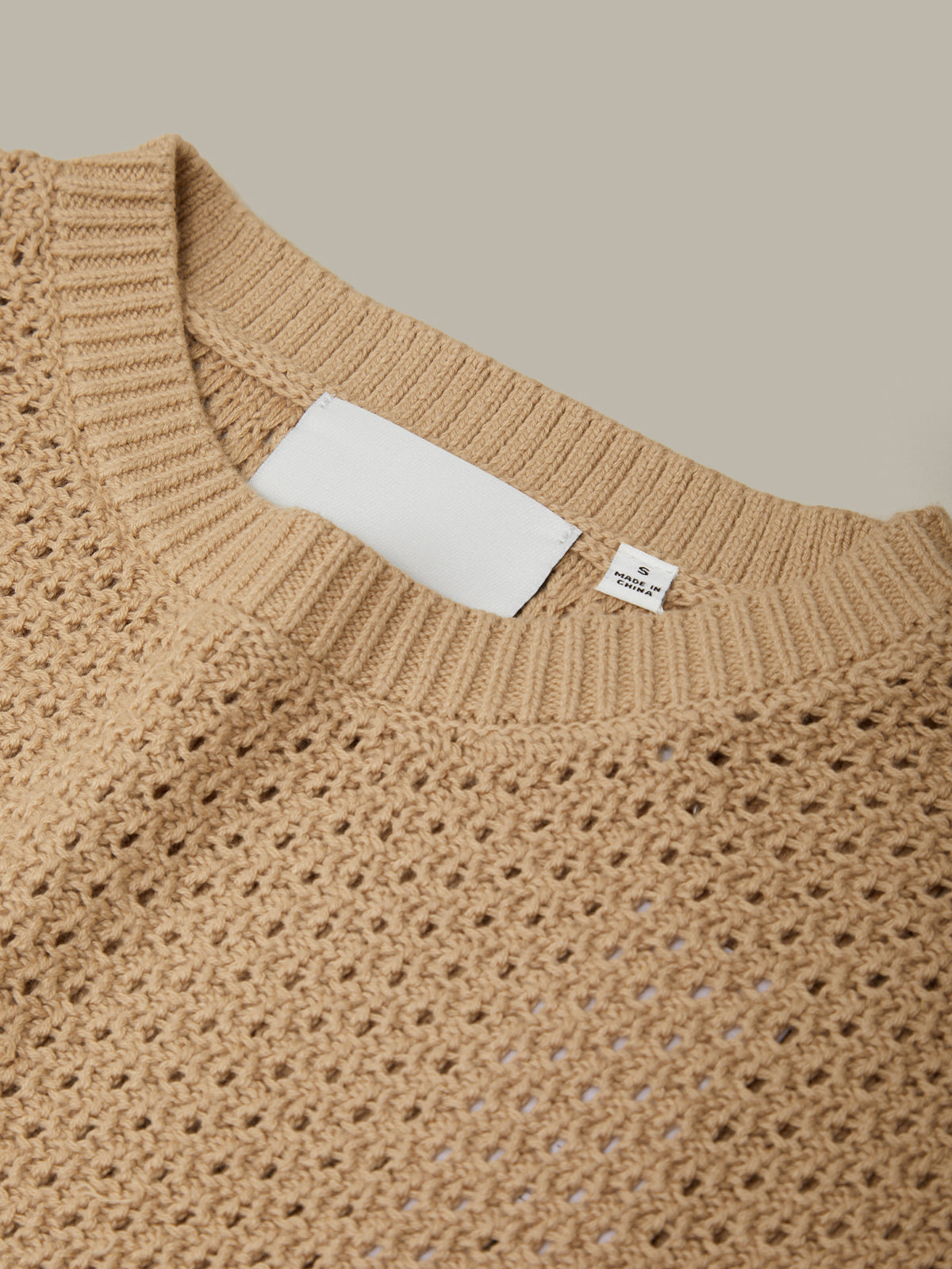 Close-up of a beige knitted sweater with brand labels on a neutral background
