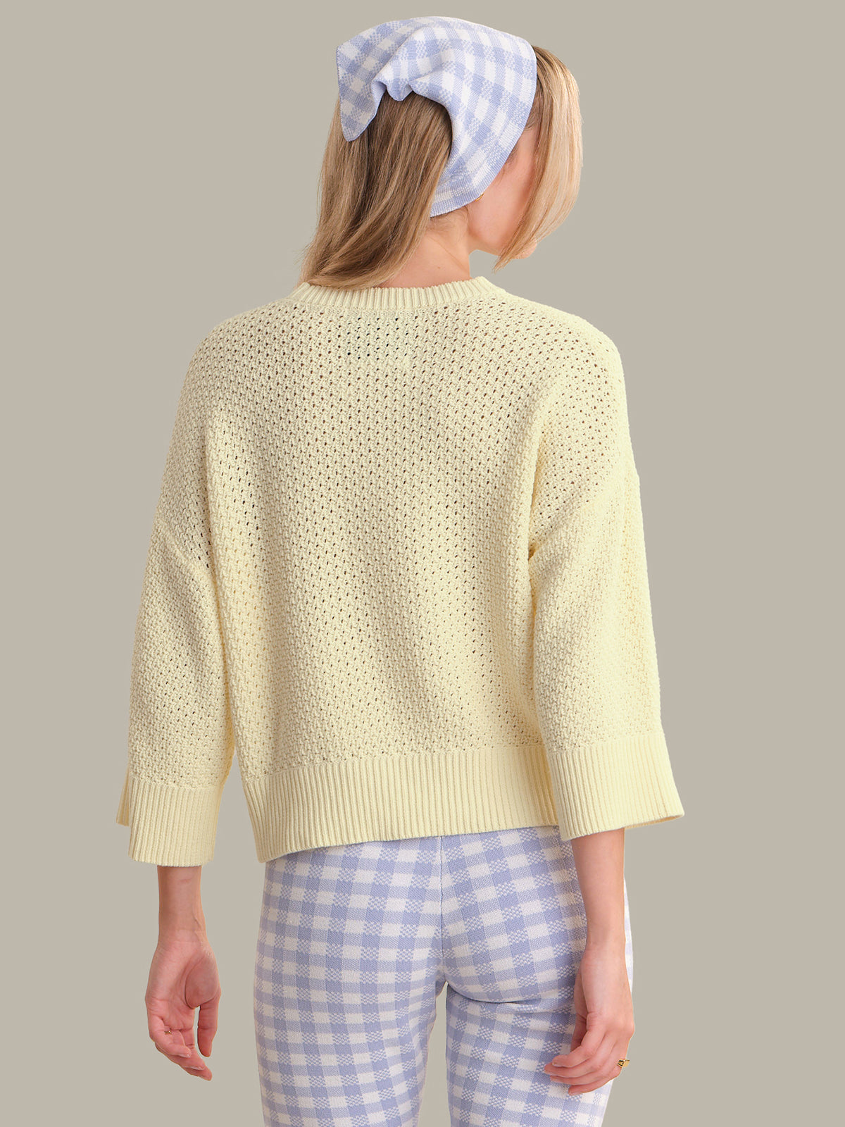 Person wearing a light yellow textured sweater and blue checkered headscarf on a plain background