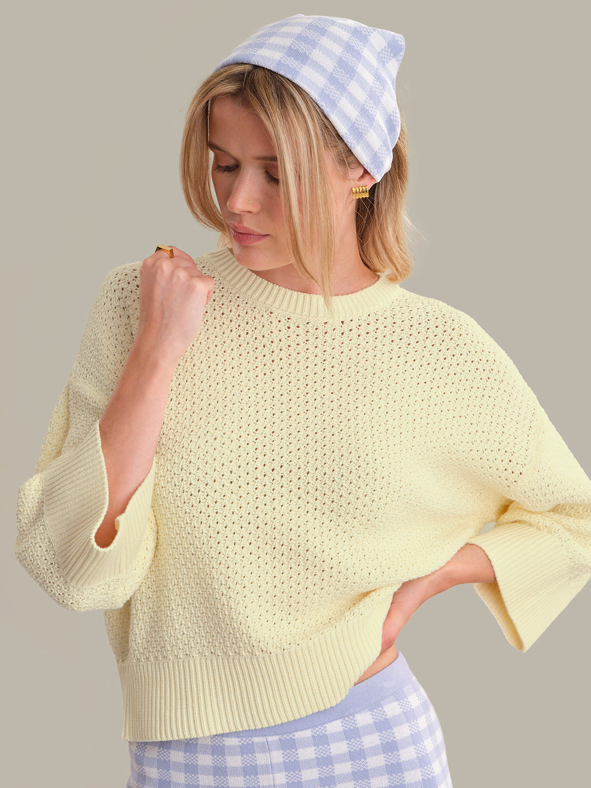 Woman wearing a light yellow sweater and blue checkered headband, standing against a neutral background.