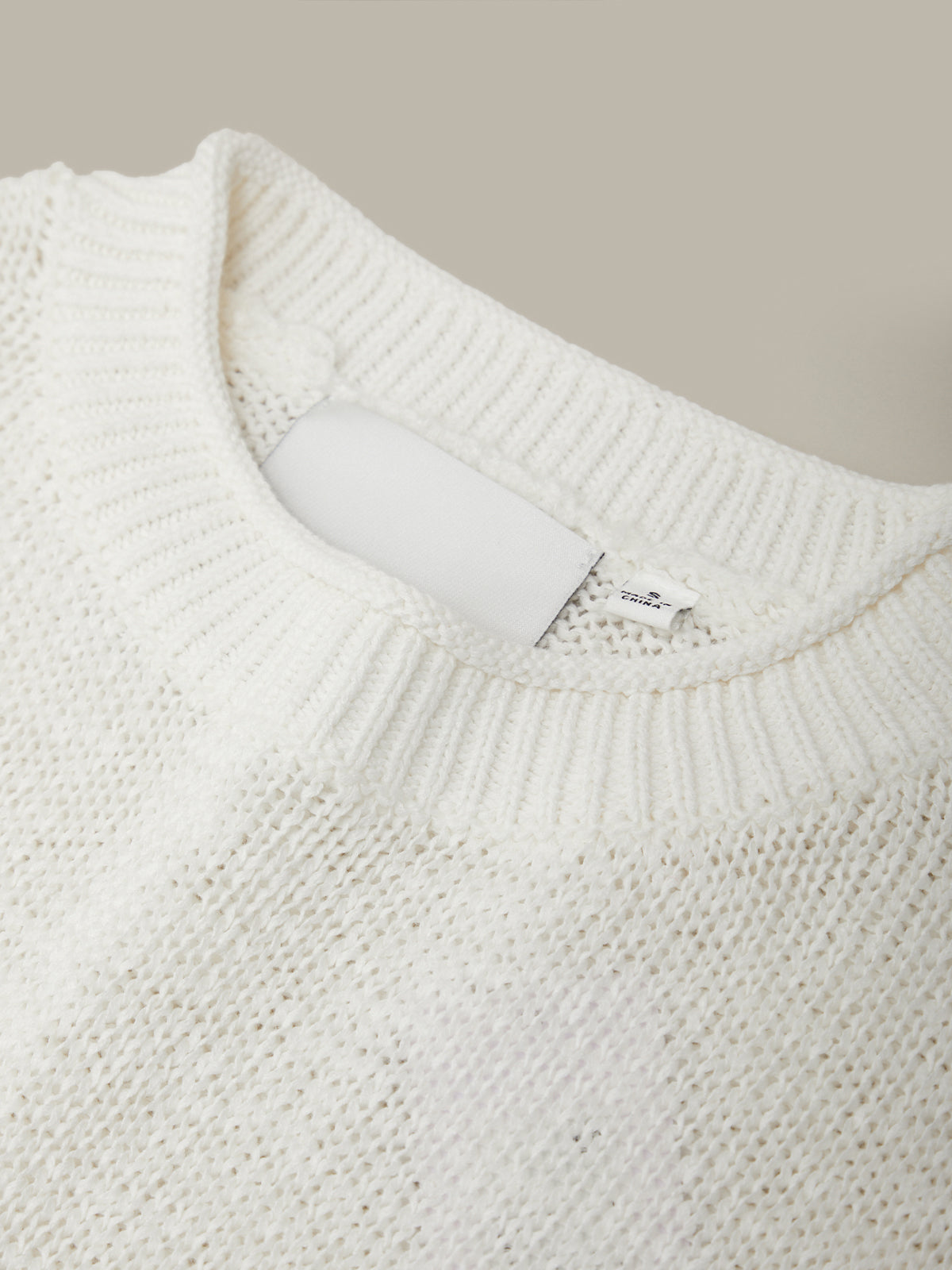 Close-up of a white knit sweater with a brand label on a beige background