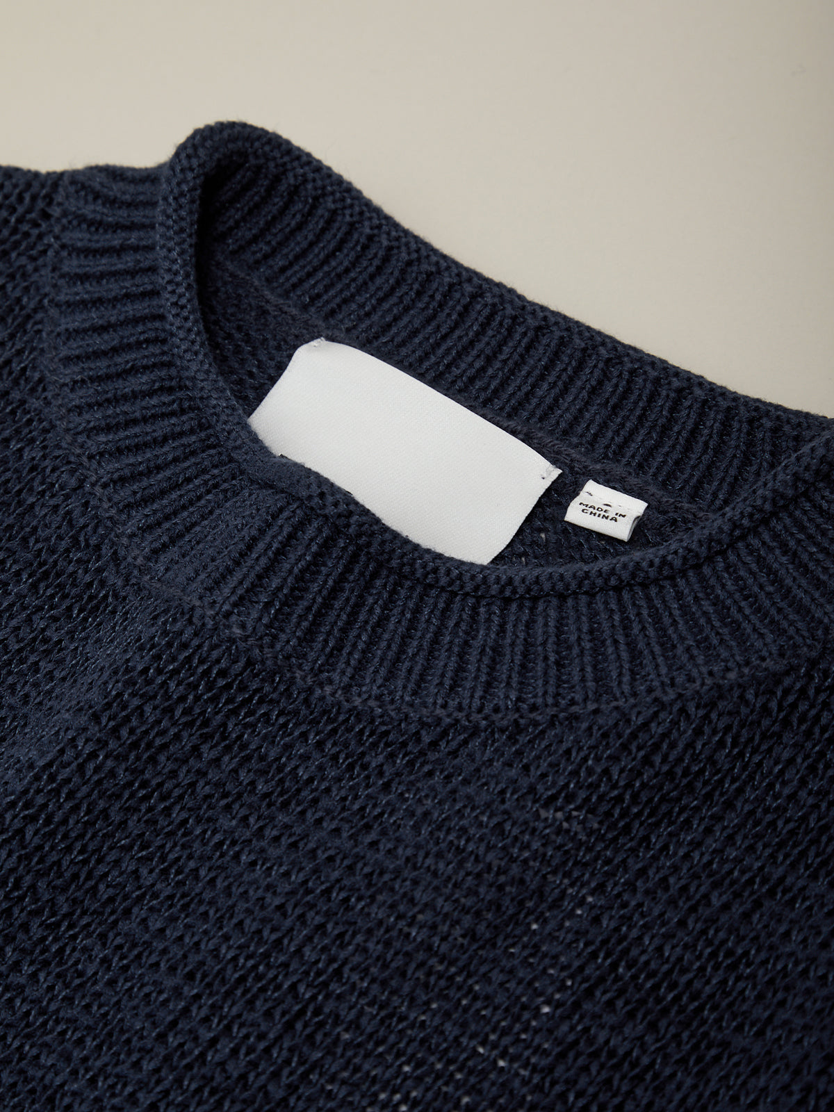Navy blue sweater with a visible brand label on a beige background