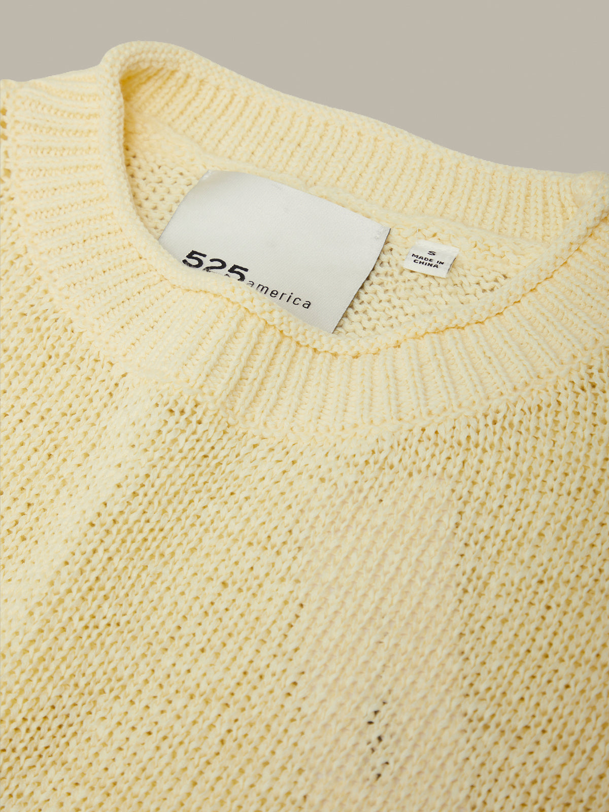 Close-up of a yellow sweater with a brand label on a neutral background