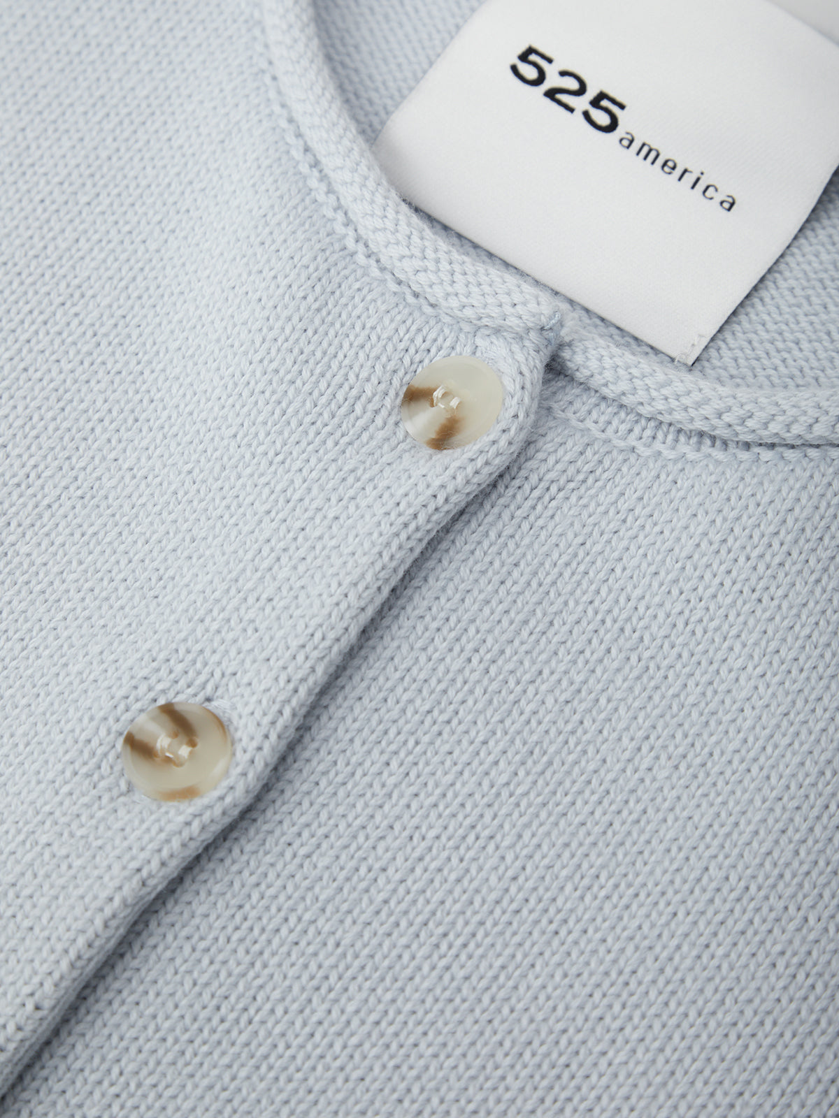Close-up of a light gray sweater with buttons and a visible brand label.