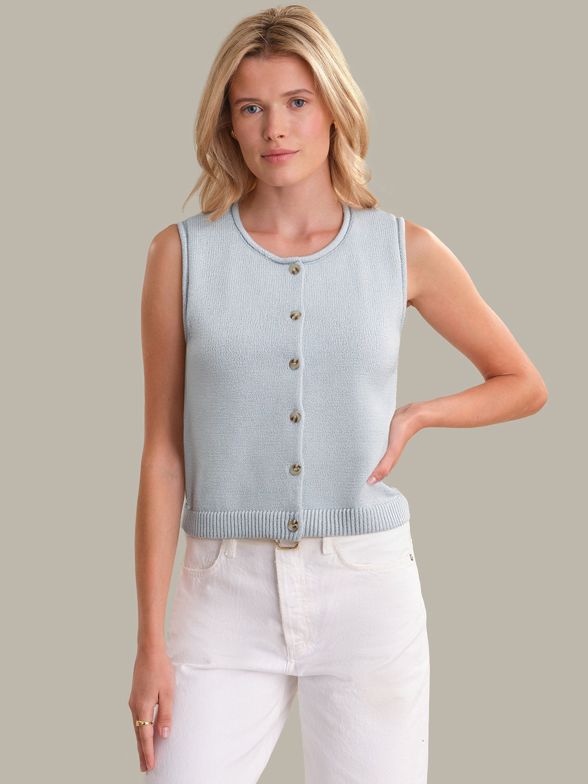 Woman wearing a light blue sleeveless cardigan over a white top against a neutral background