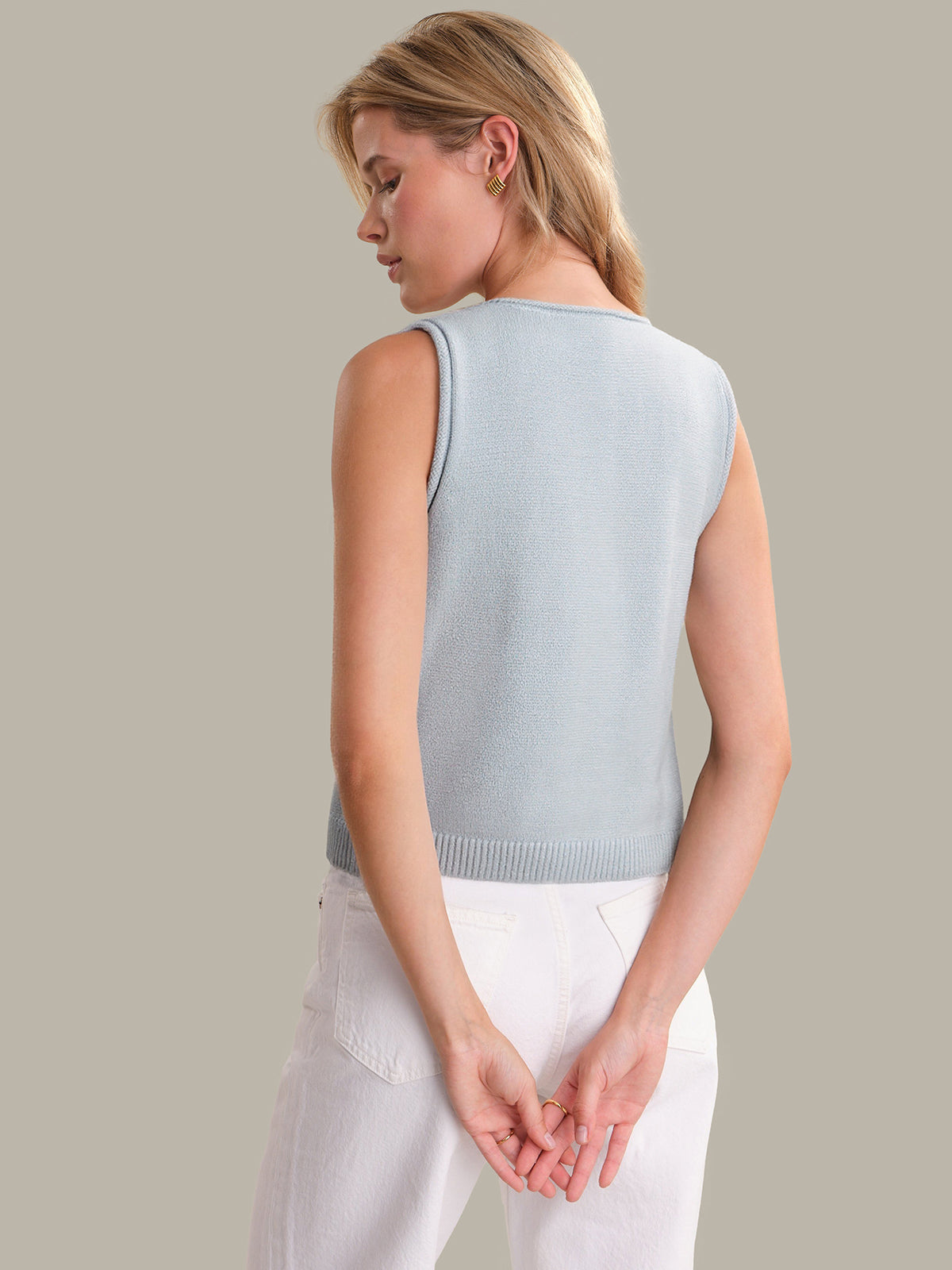 Woman wearing a light blue sleeveless sweater against a neutral background