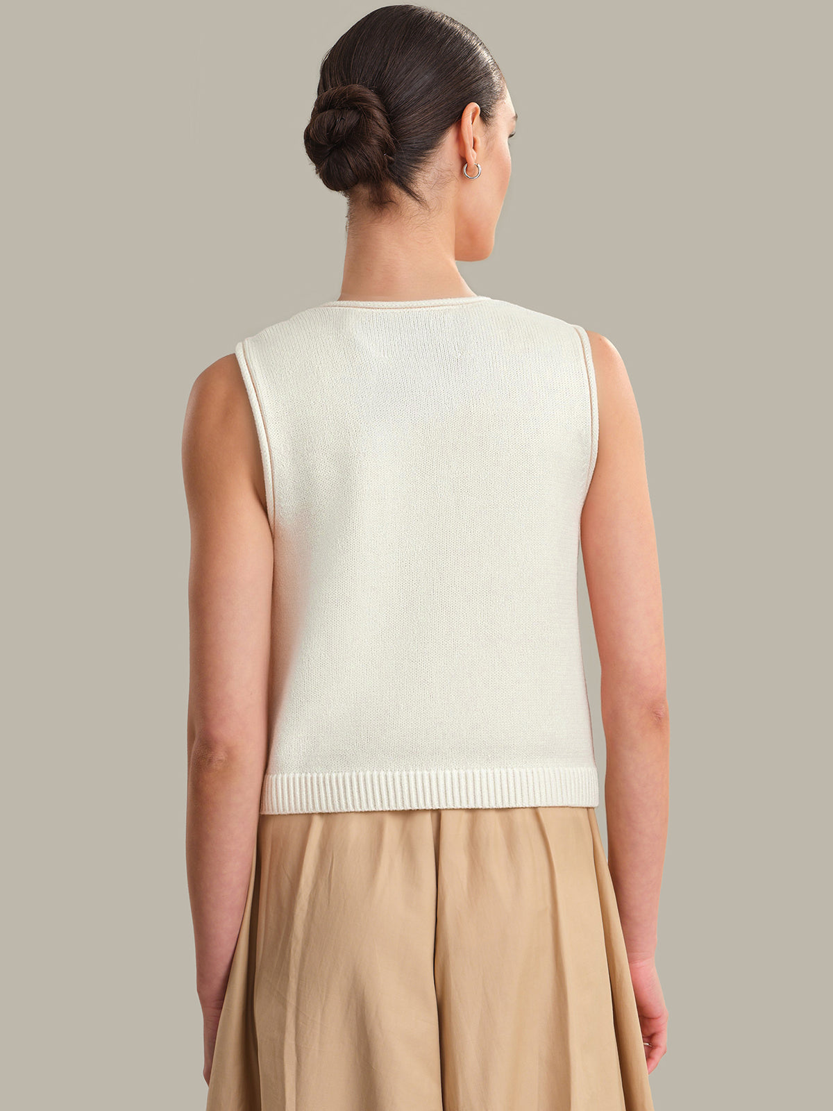 Woman wearing a cream sleeveless sweater vest against a neutral background