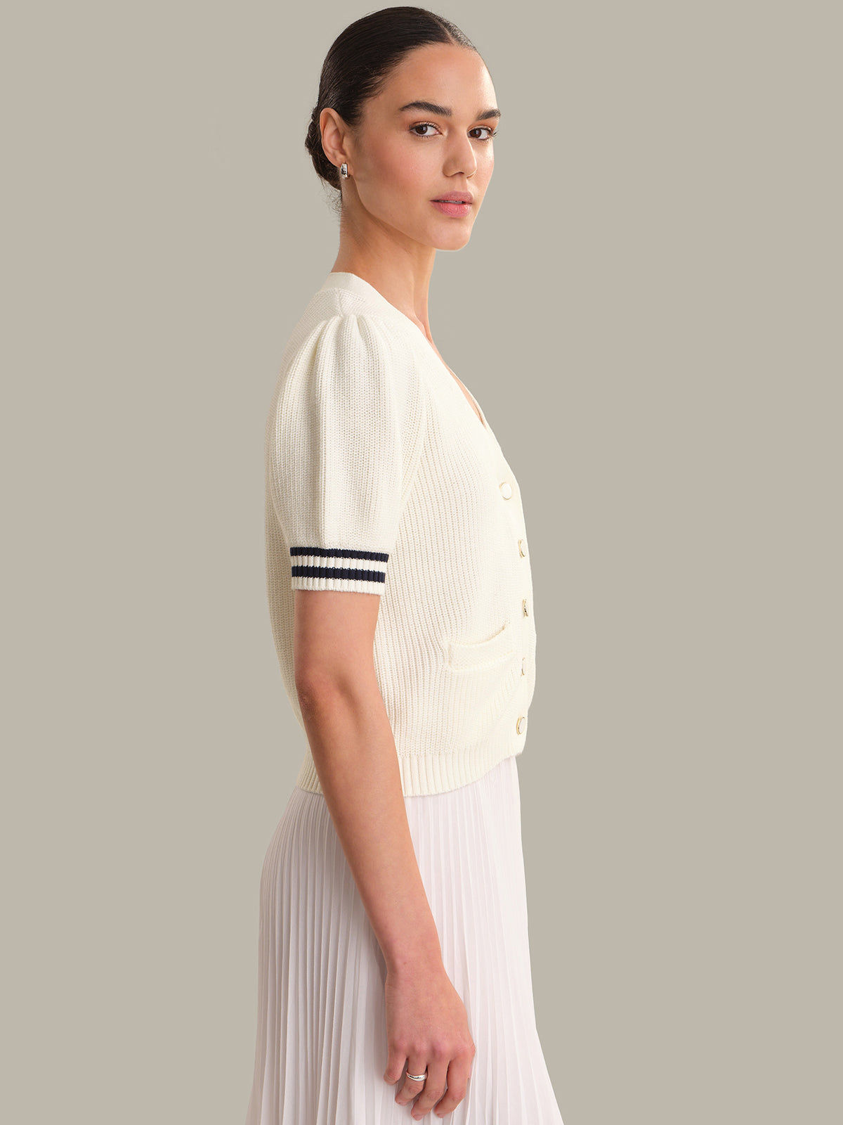 Woman wearing a white ribbed knit cardigan with black trim on a gray background