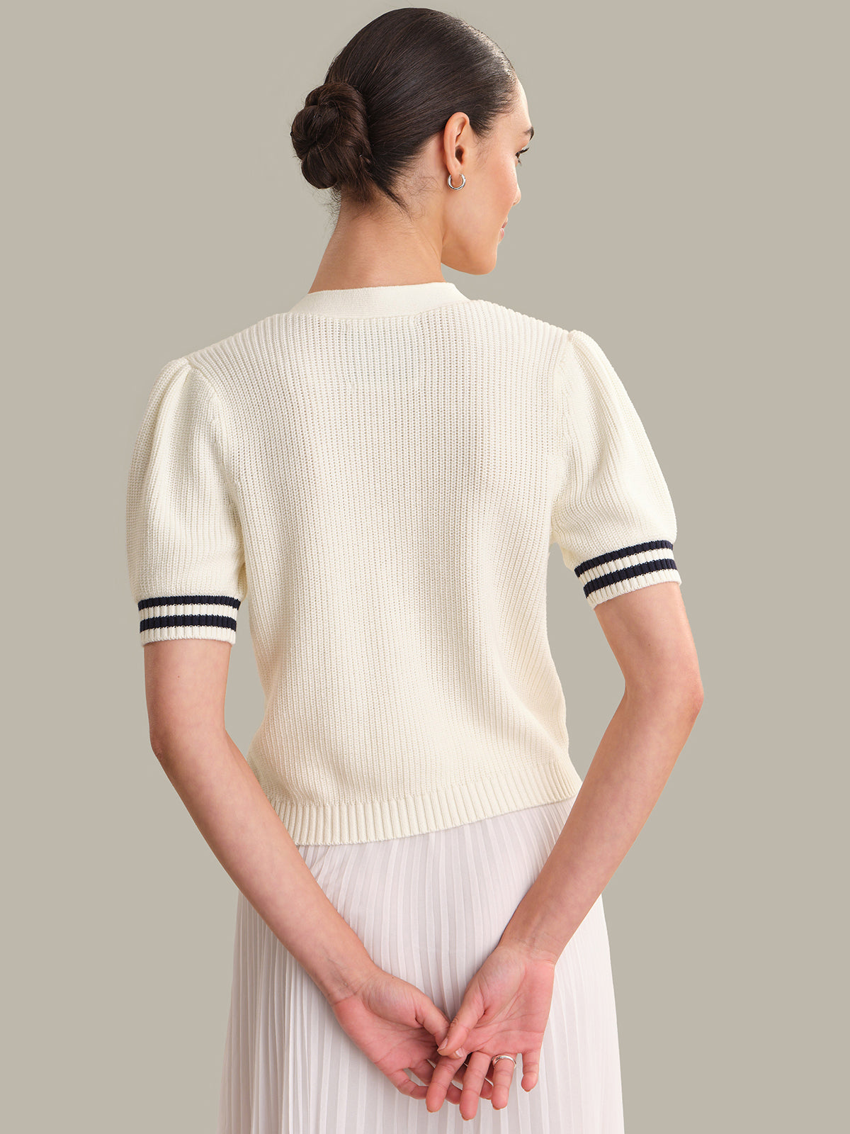 Woman wearing a cream-colored short-sleeve sweater with black stripes on a gray background