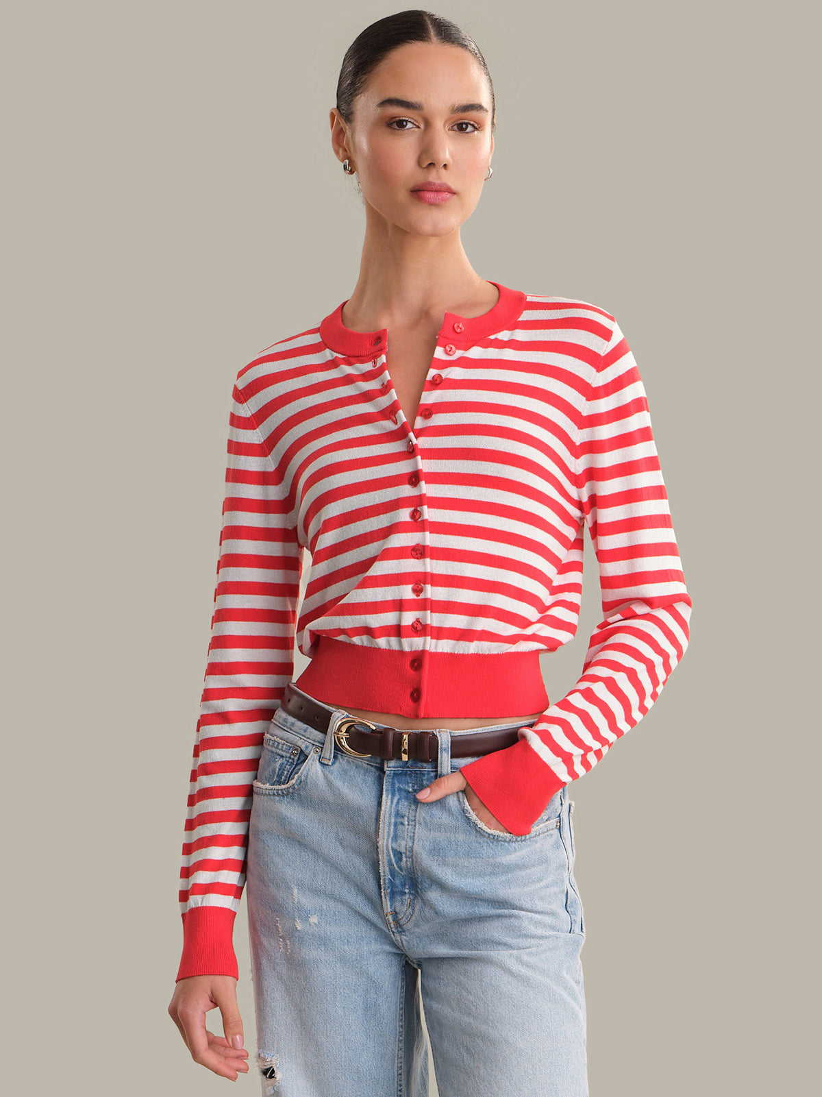 Woman wearing a red and white striped cardigan with blue jeans on a gray background