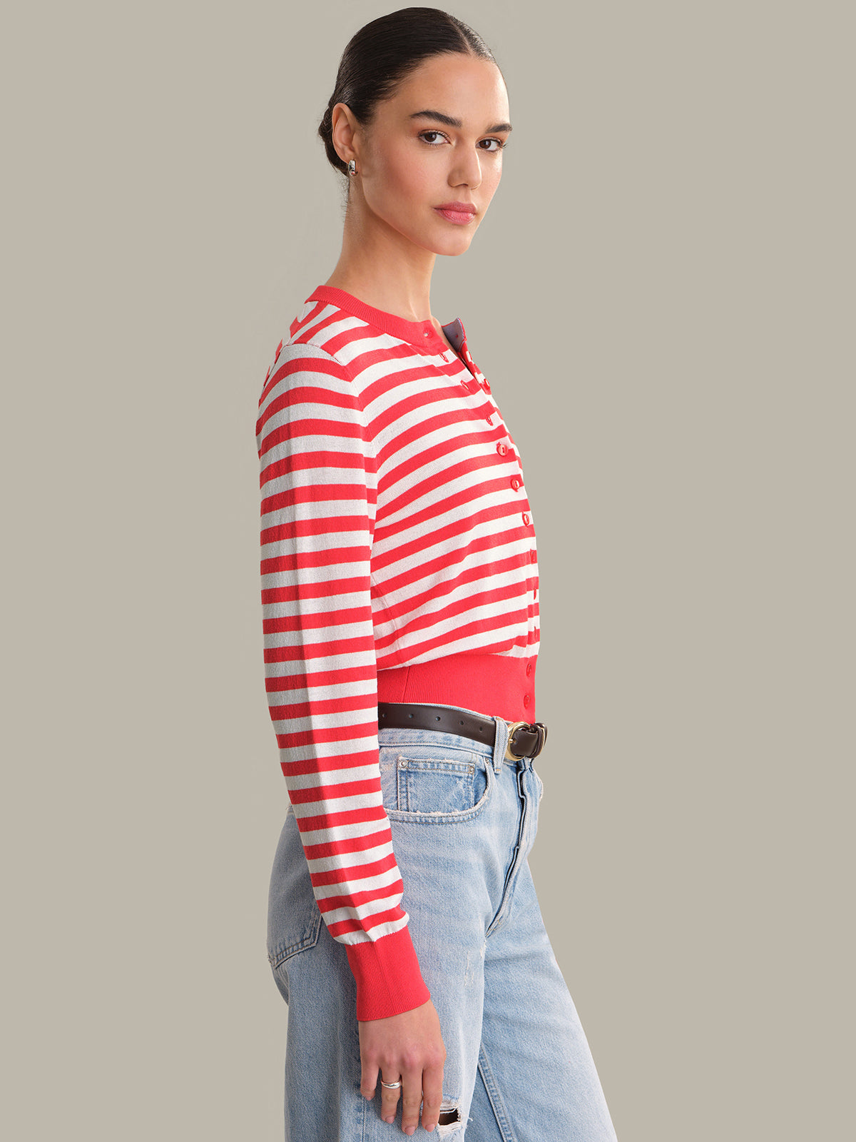 Person wearing a red and white striped cardigan with blue jeans on a gray background