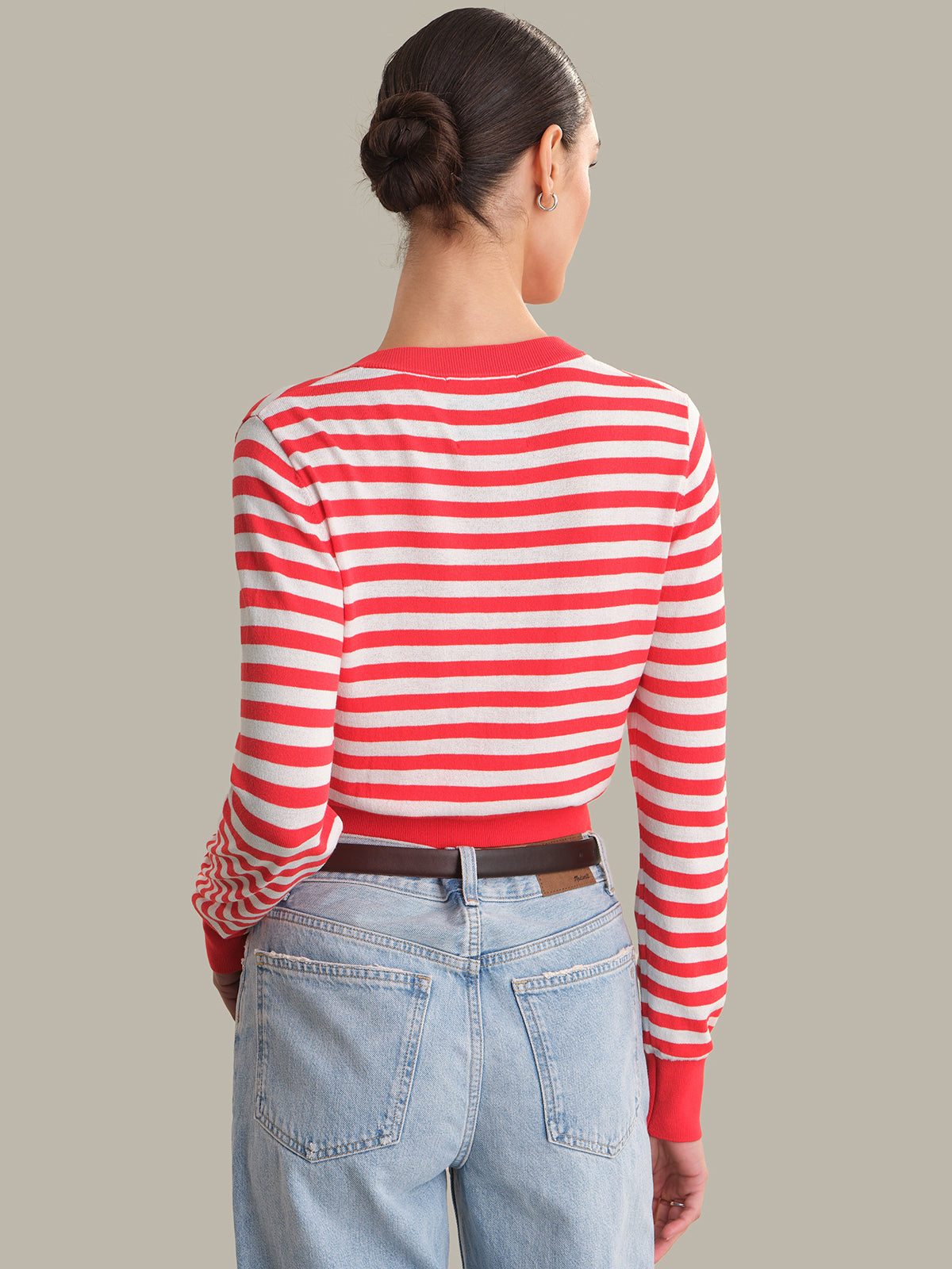 Person wearing a red and white striped cardigan with blue jeans on a neutral background