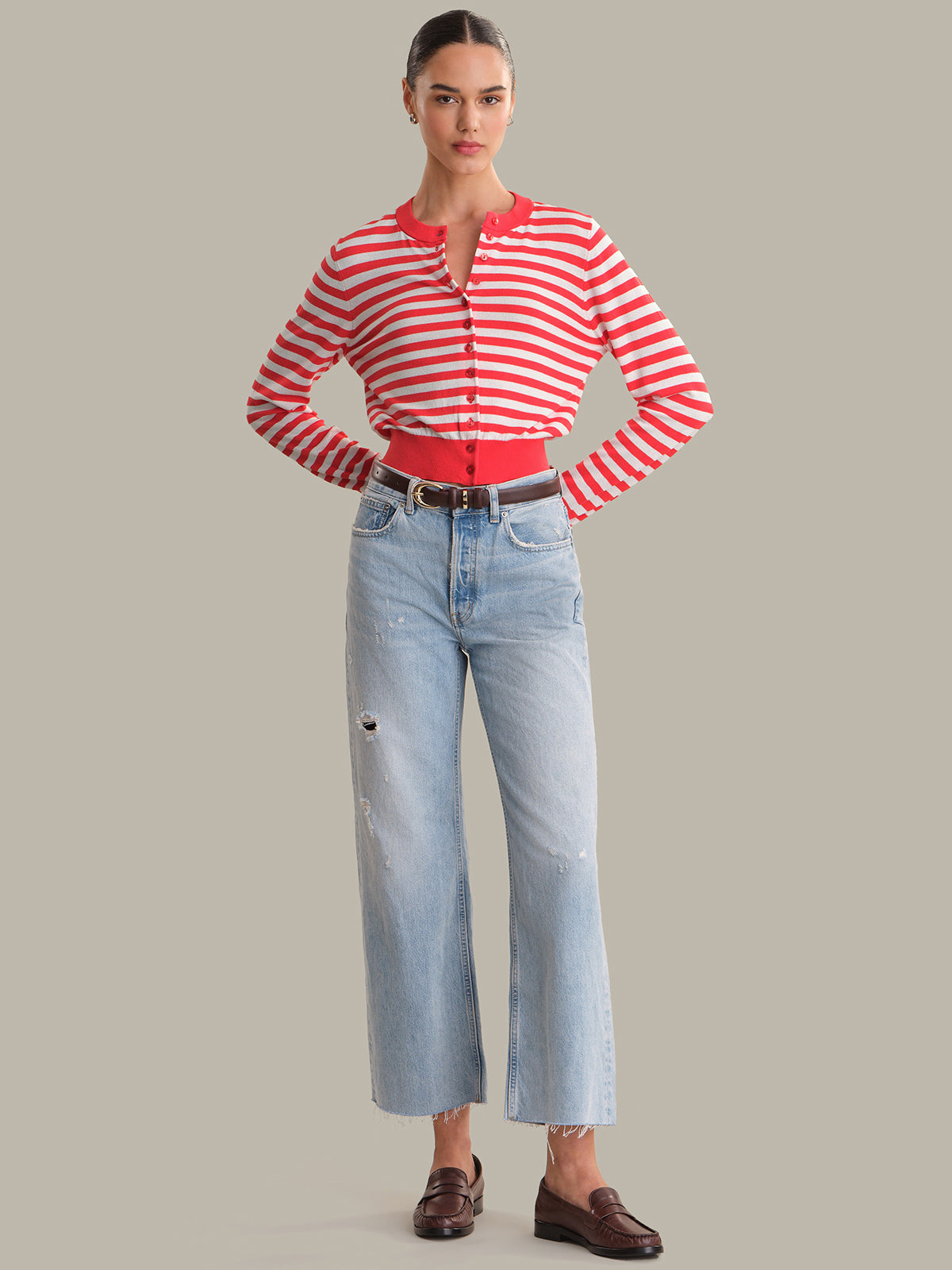 Woman wearing a red and white striped cardigan and light blue jeans on a gray background