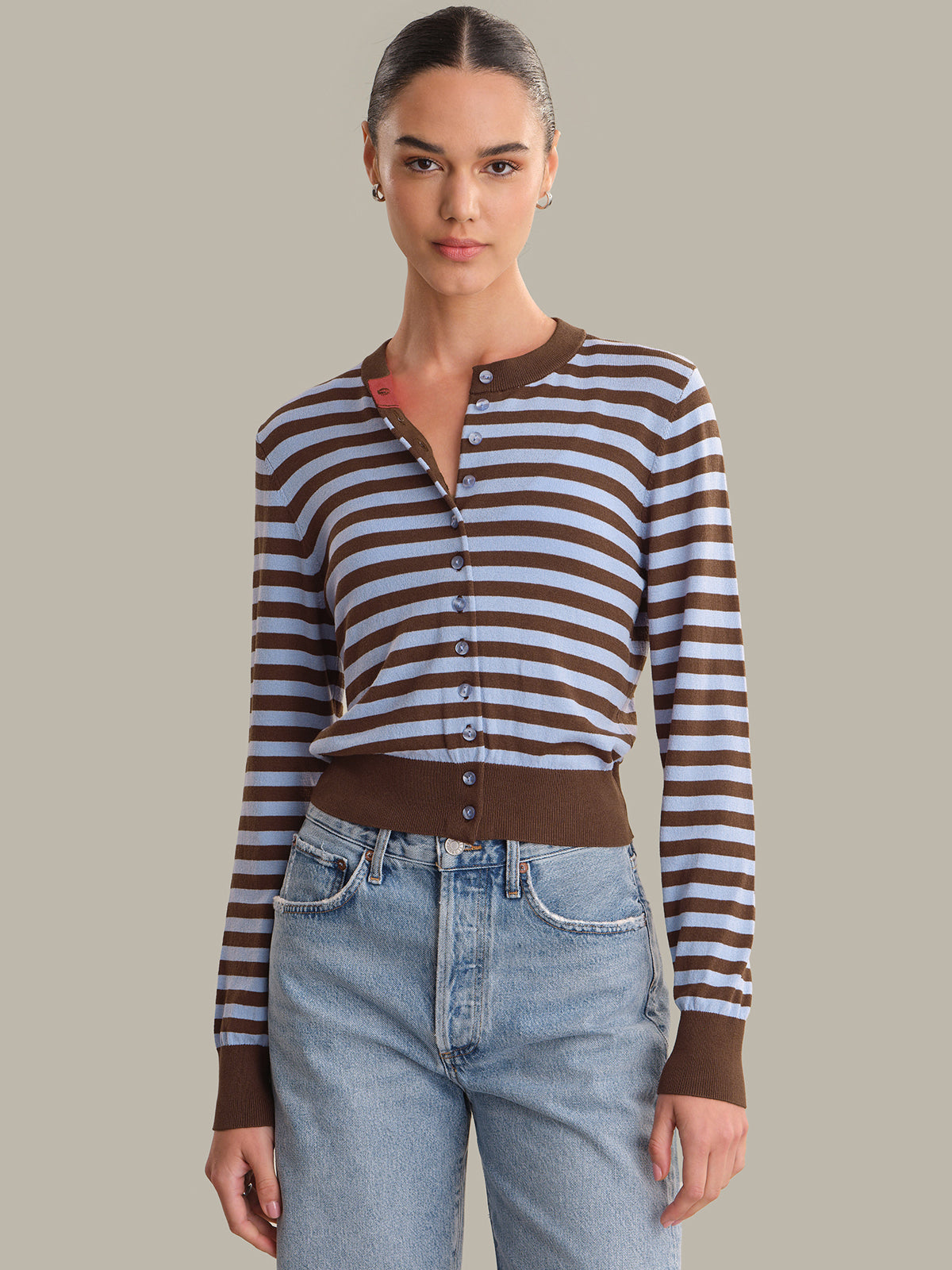 Woman wearing a brown and white striped cardigan with blue jeans on a plain background