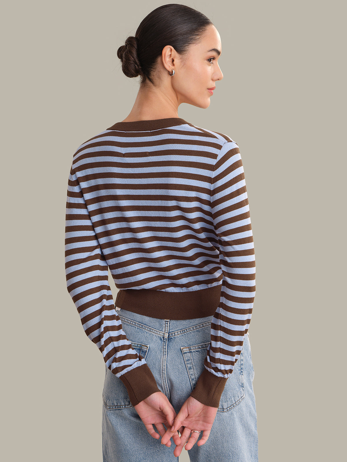 Woman wearing a brown and white striped cardigan with blue jeans on a plain background
