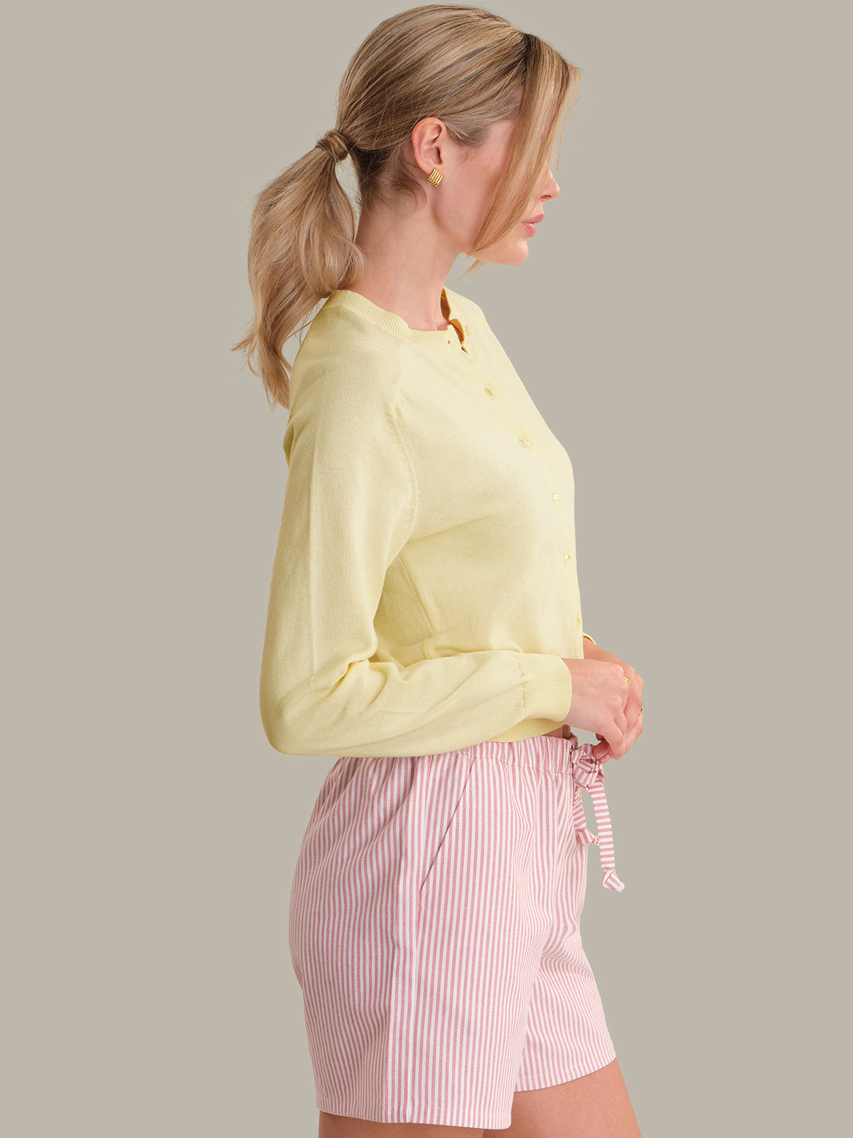 Woman wearing a light yellow shirt and pink striped shorts on a plain background