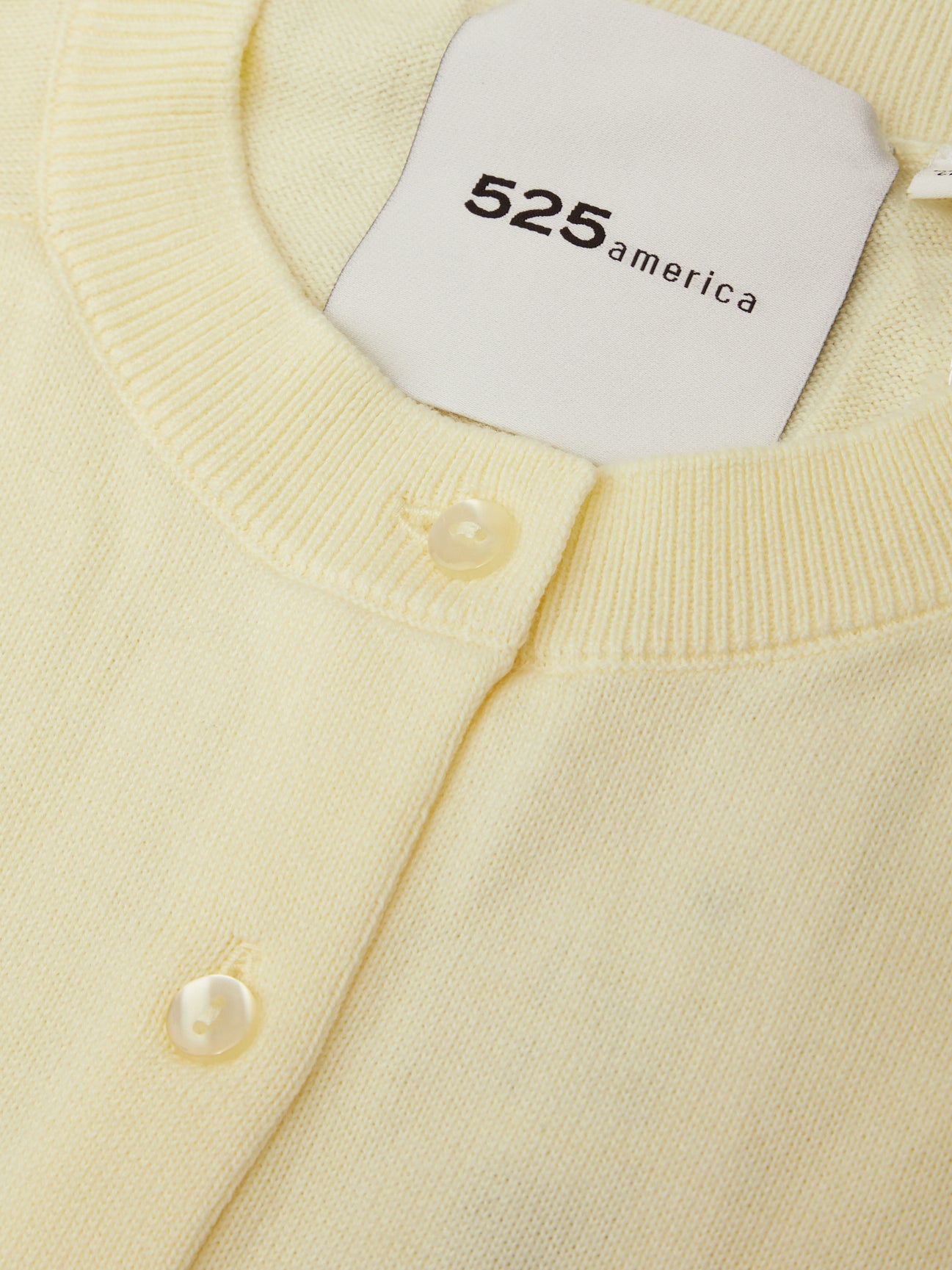Close-up of a light yellow cardigan with pearl buttons and a brand label.