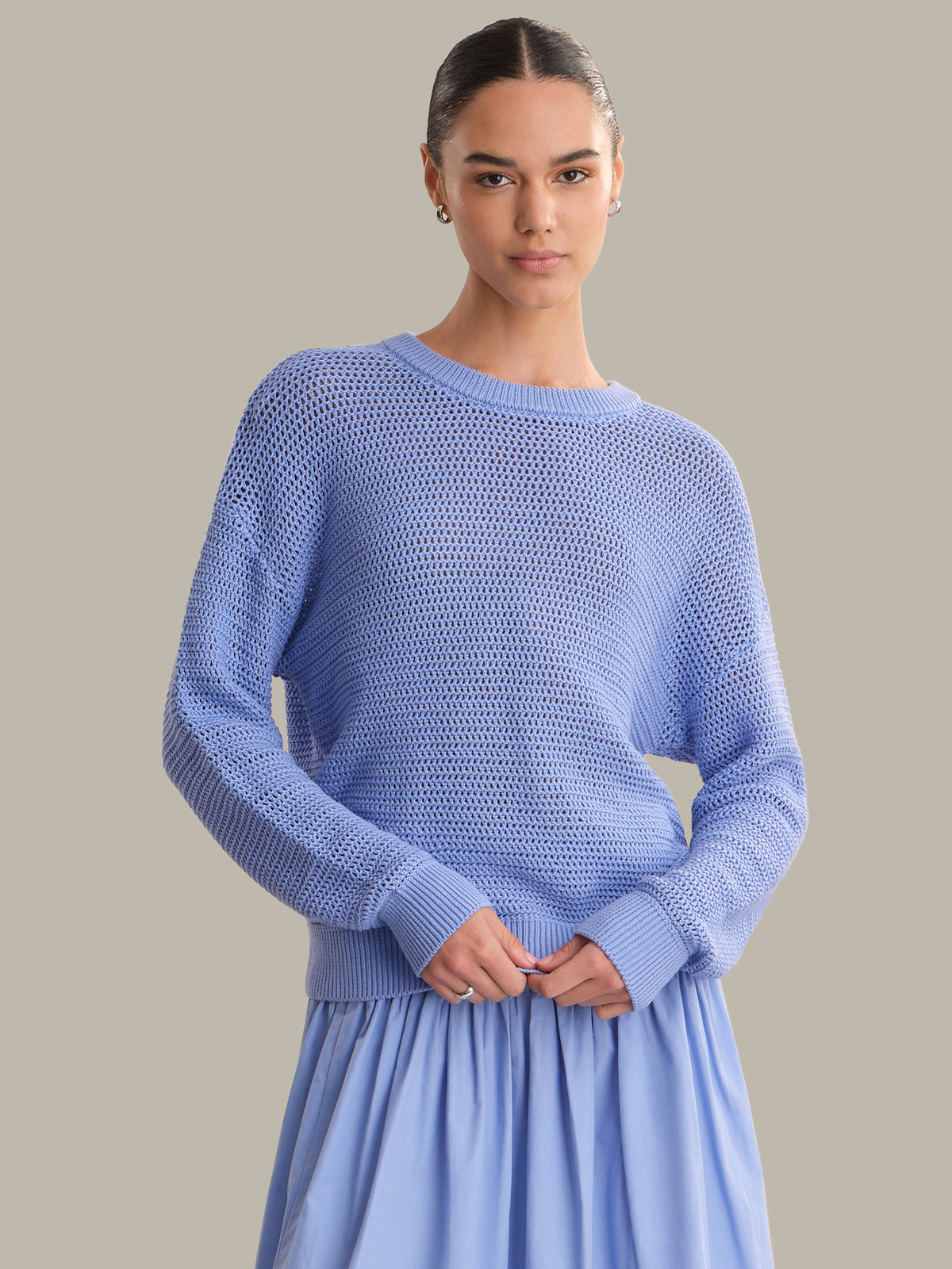 Woman wearing a light blue sweater and skirt against a neutral background
