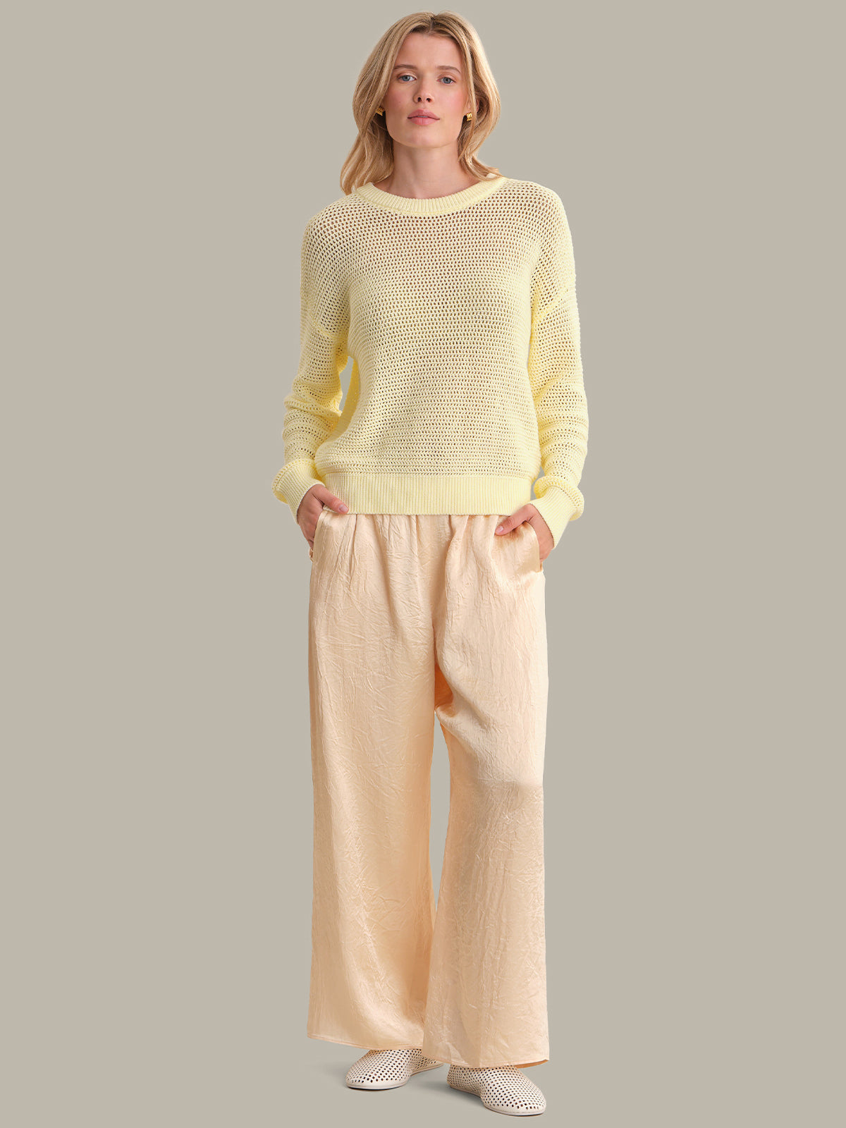Woman wearing a yellow knit sweater and beige pants on a gray background