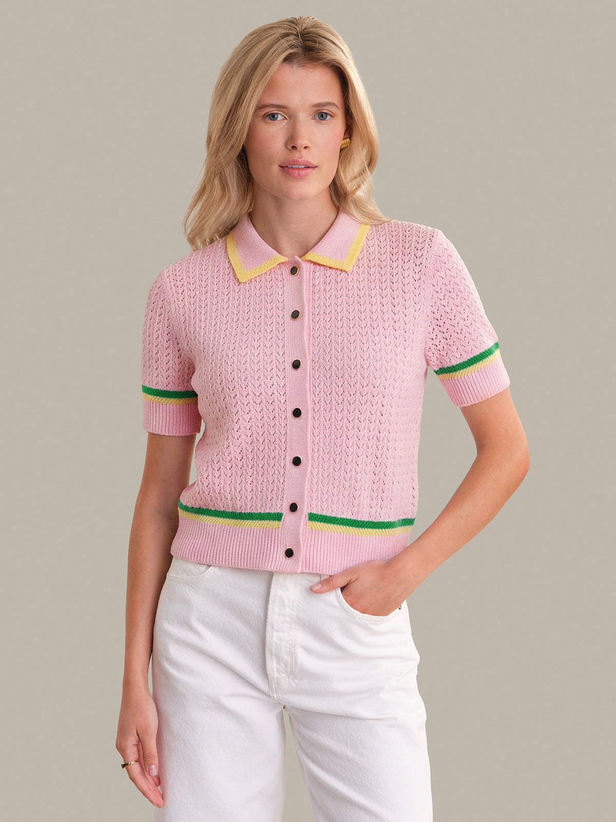 Woman wearing a pink knitted cardigan with colorful trim on a plain background