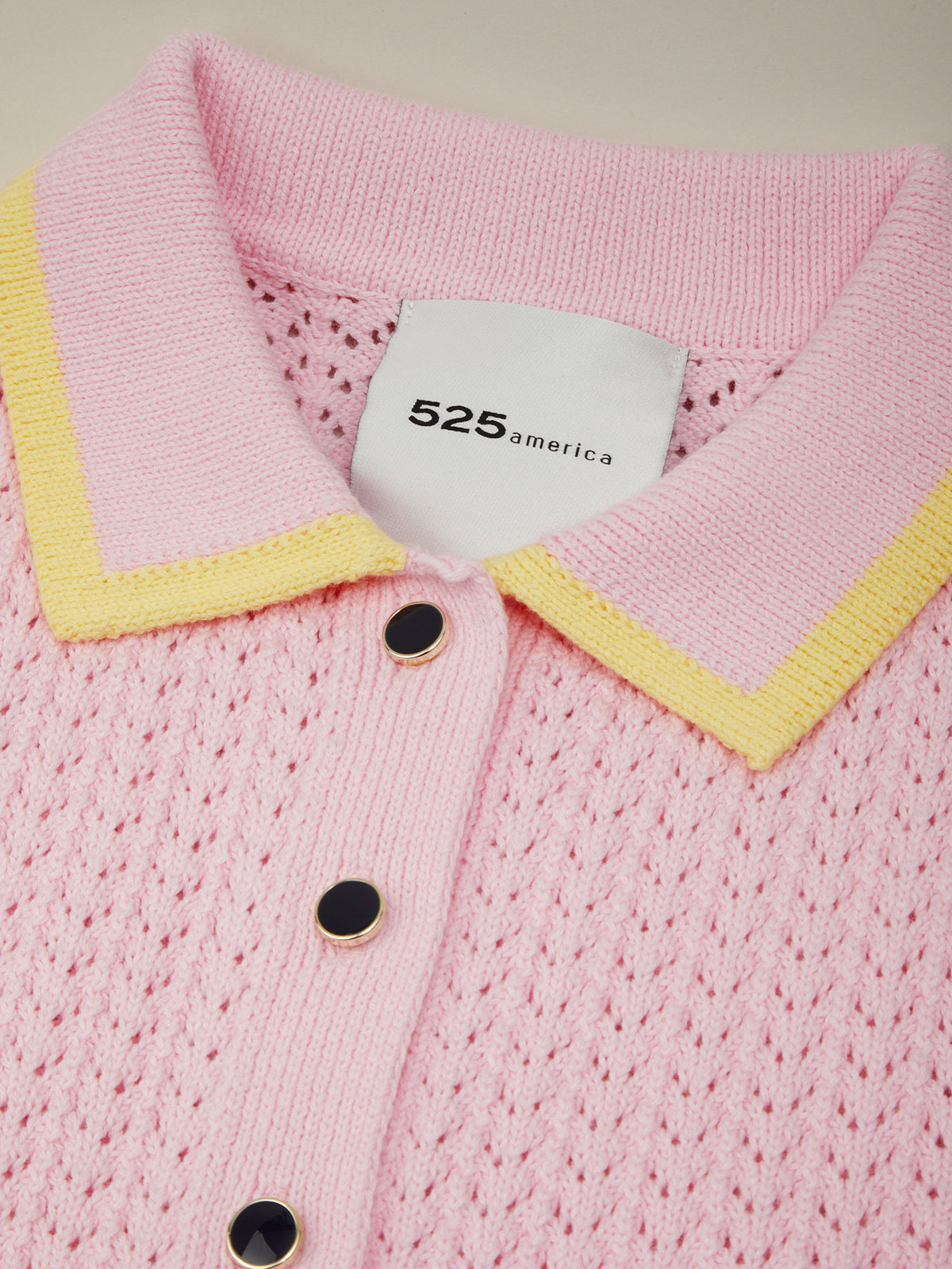 Pink cardigan with yellow trim and black buttons, featuring a brand tag.