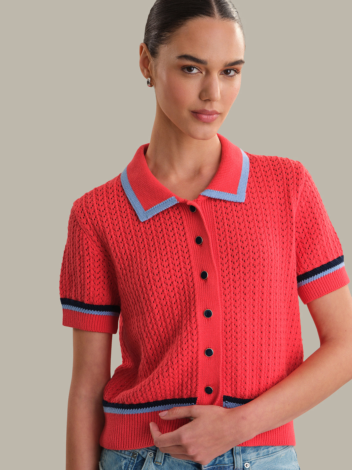 Woman wearing a red knitted polo shirt with blue trim on a neutral background