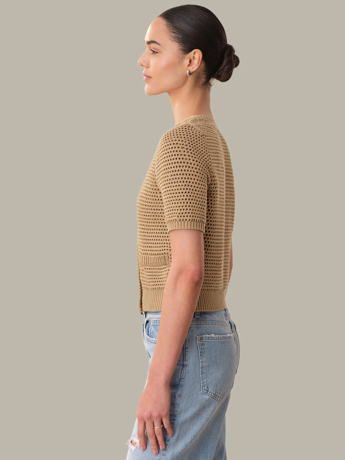 Woman wearing a beige knitted sweater and blue jeans against a plain background