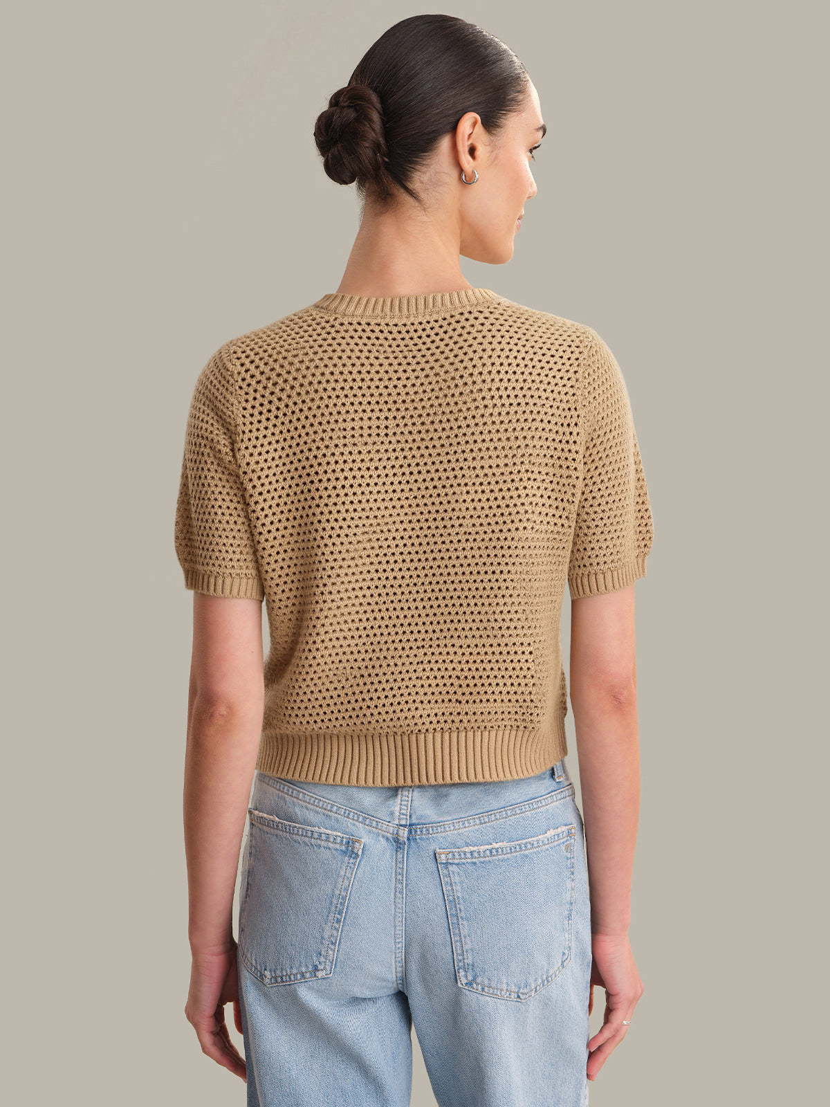 Woman wearing a beige knitted top and light blue jeans on a neutral background