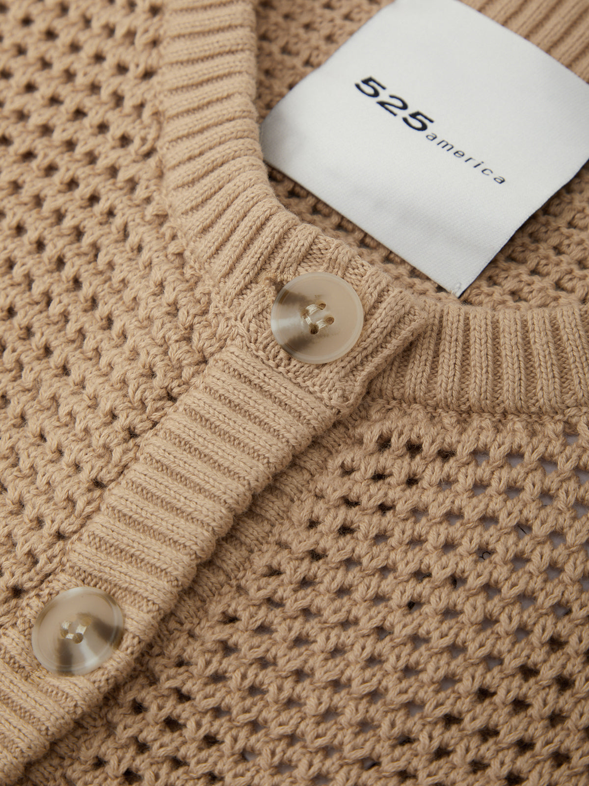 Close-up of a beige knitted sweater with a brand tag displaying '525 America'.