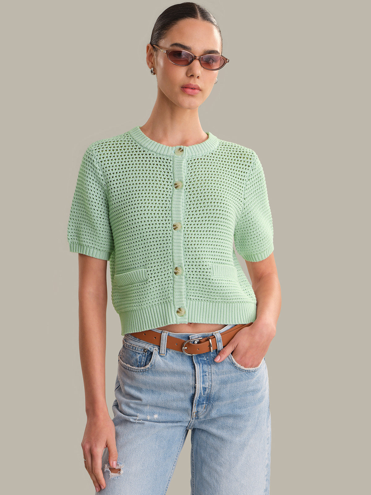 Woman wearing a light green knitted cardigan and blue jeans against a neutral background