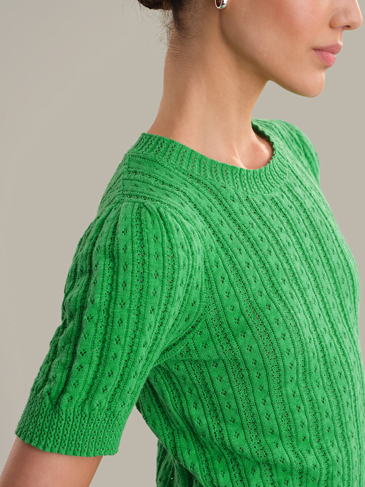 Green knitted sweater worn by a person on a neutral background