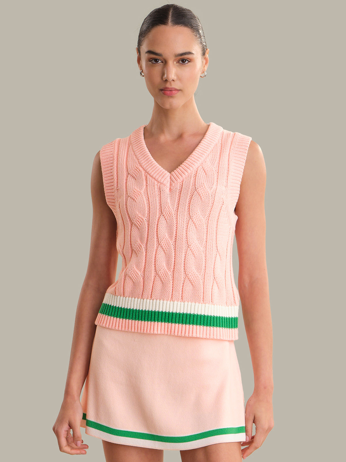 Woman wearing a pink sleeveless sweater with green and white trim on a gray background