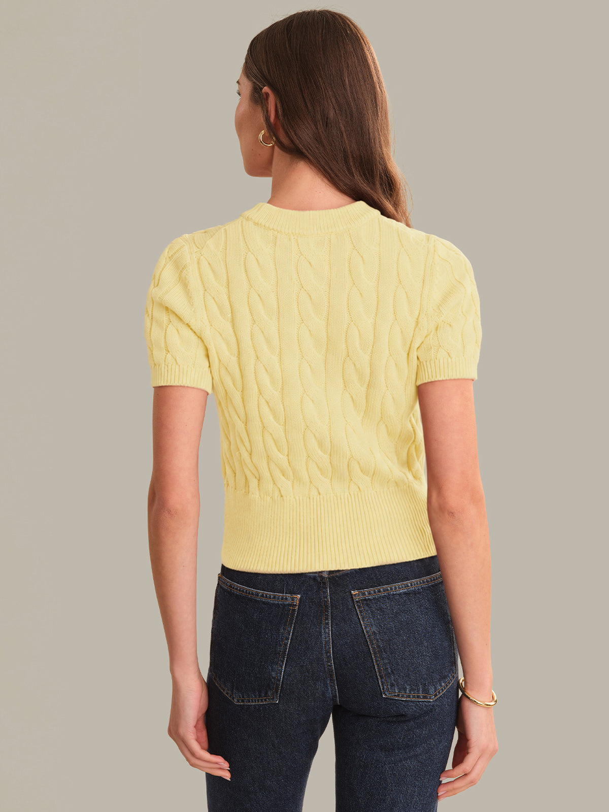 Woman wearing a yellow cable knit sweater and dark jeans on a plain background
