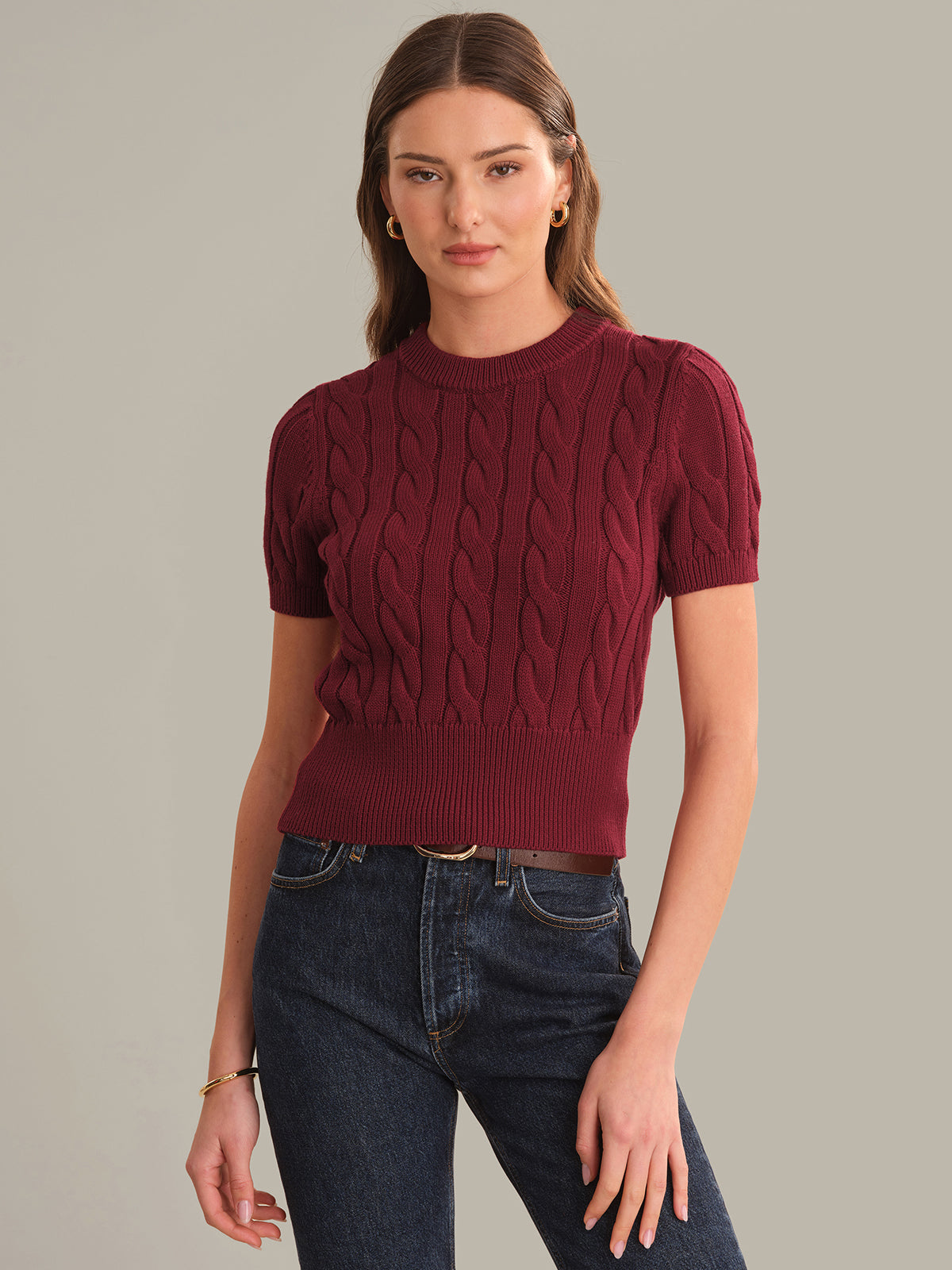 Woman wearing a maroon cable knit sweater and blue jeans on a gray background