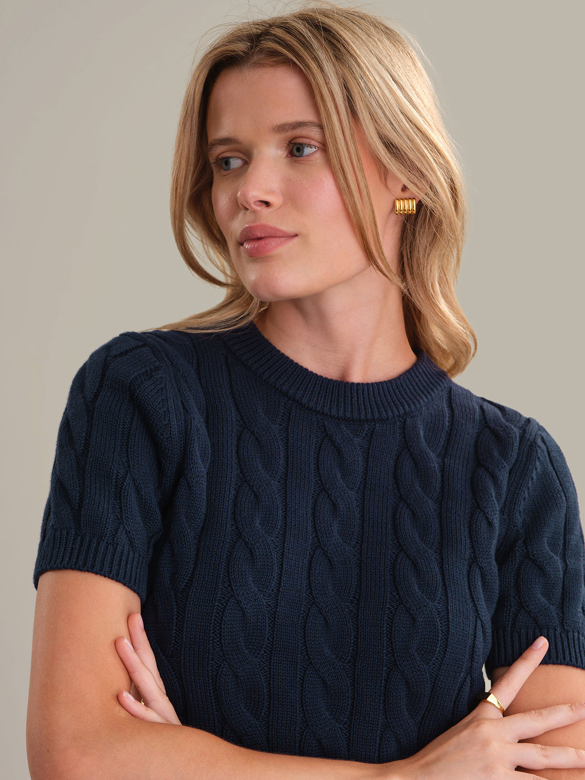 Woman wearing a navy blue cable knit sweater against a neutral background