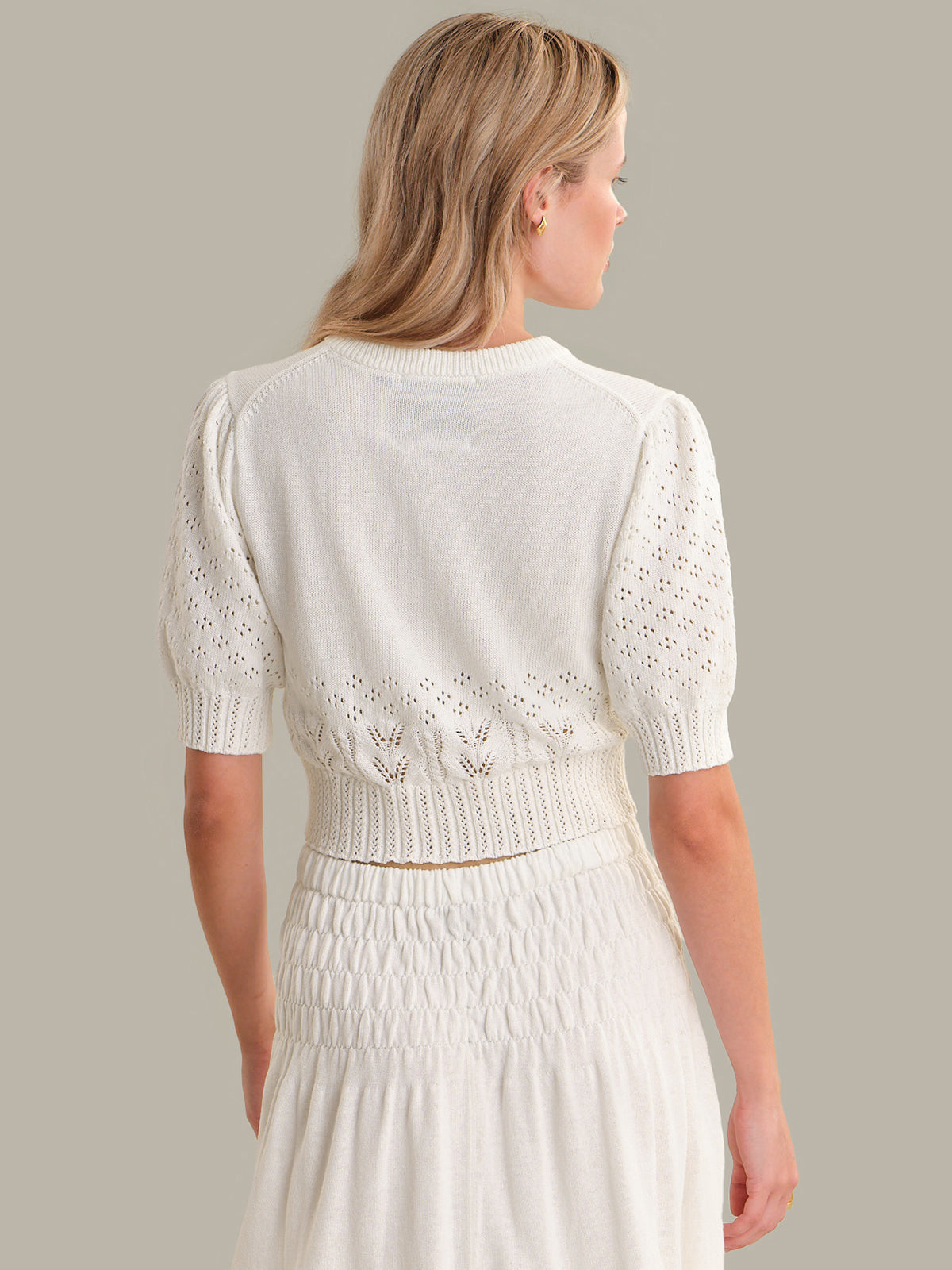 Woman wearing a white dress with a textured top and smocked waist on a plain background