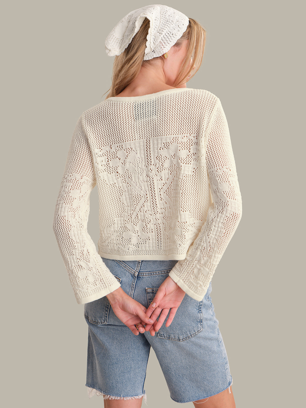 Person wearing a white lace cardigan and denim shorts on a plain background