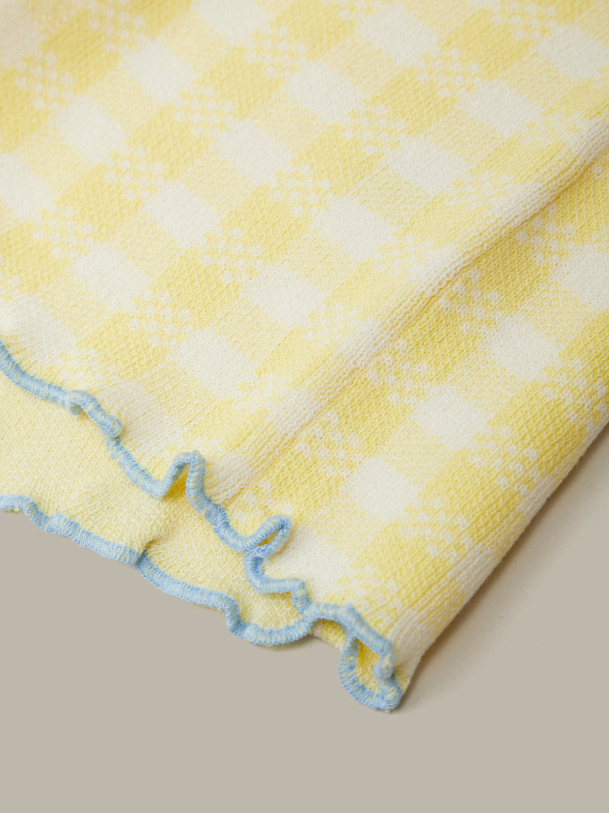 Yellow and white checkered blanket with blue trim on a neutral background