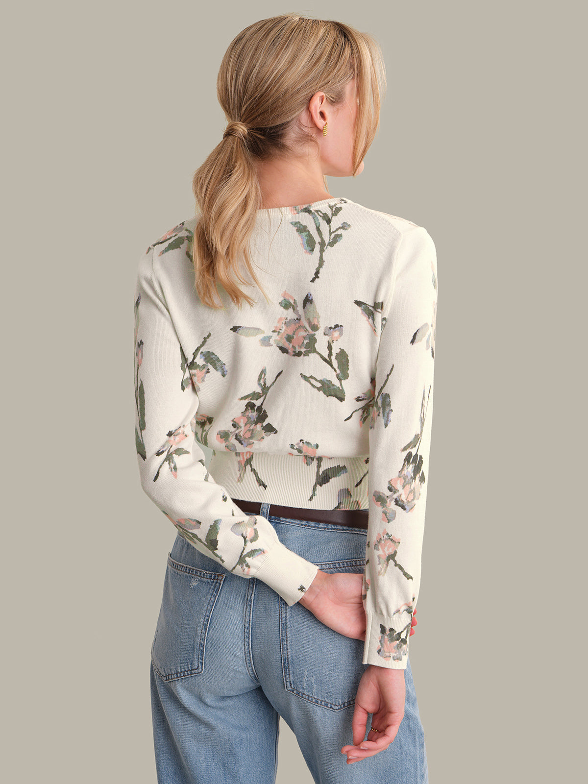 Woman wearing a floral long-sleeve cardigan and blue jeans on a plain background