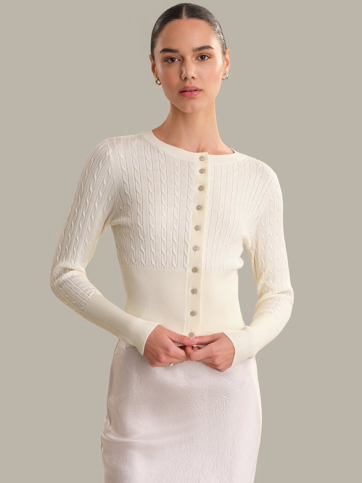 Woman wearing a white ribbed cardigan with button details on a gray background
