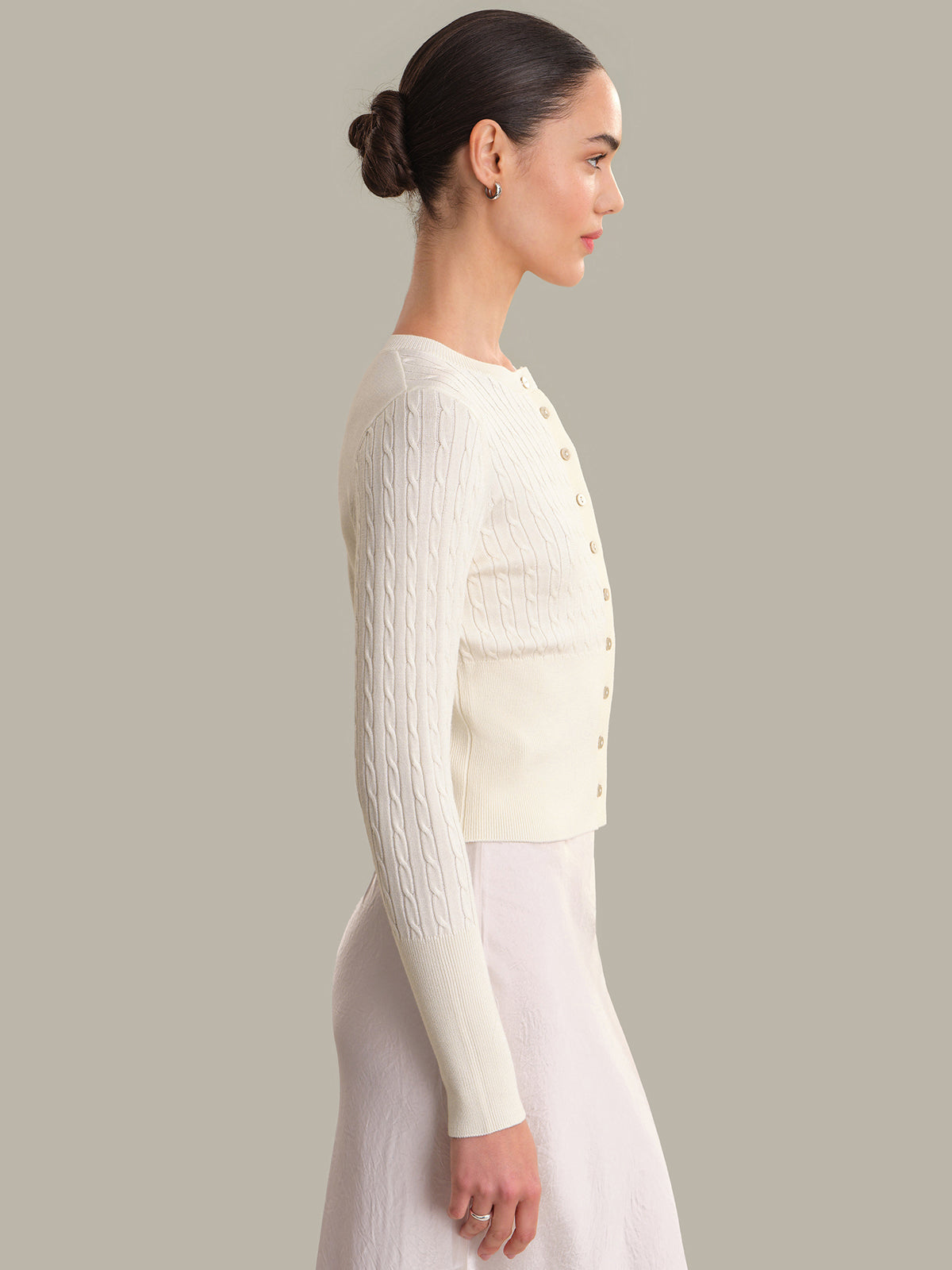 Woman wearing a white cable knit cardigan against a plain background