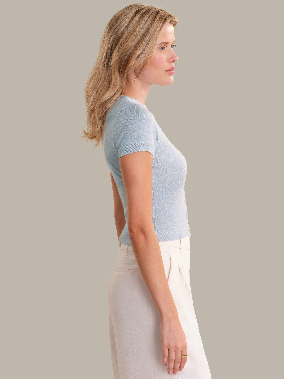 Woman wearing a light blue open-back top and white pants against a plain background