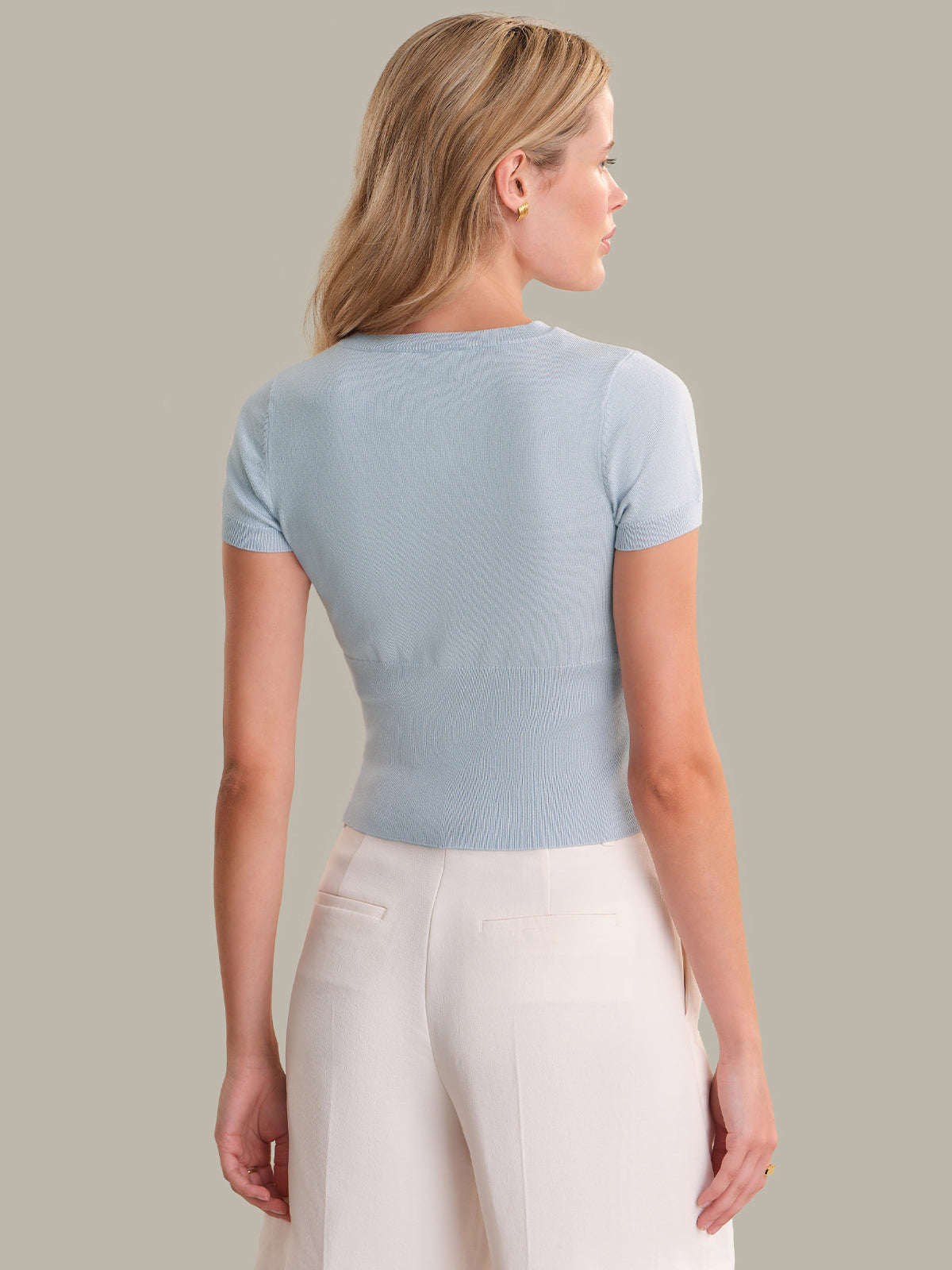 Woman wearing a light blue short-sleeve top and white pants on a neutral background