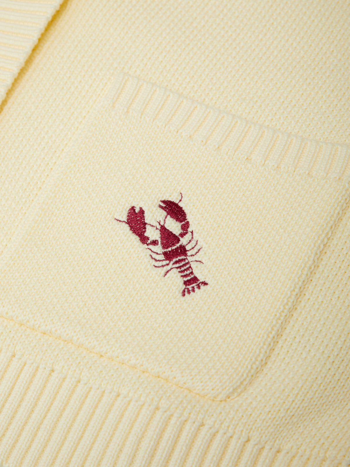 Close-up of a beige knitted blanket with a red lobster emblem.