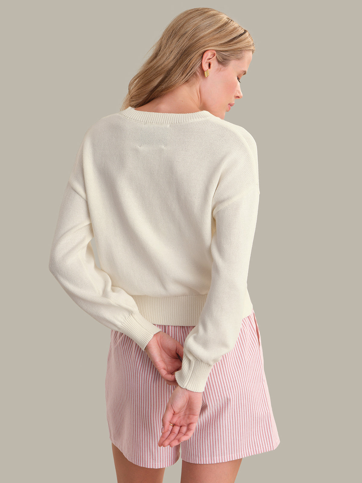 Woman wearing a white sweater and pink skirt on a plain background