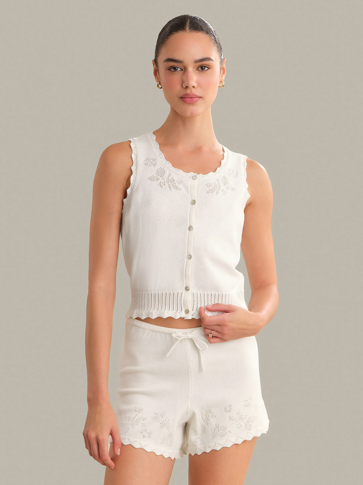 Woman wearing a white sleeveless top and shorts with lace details on a gray background