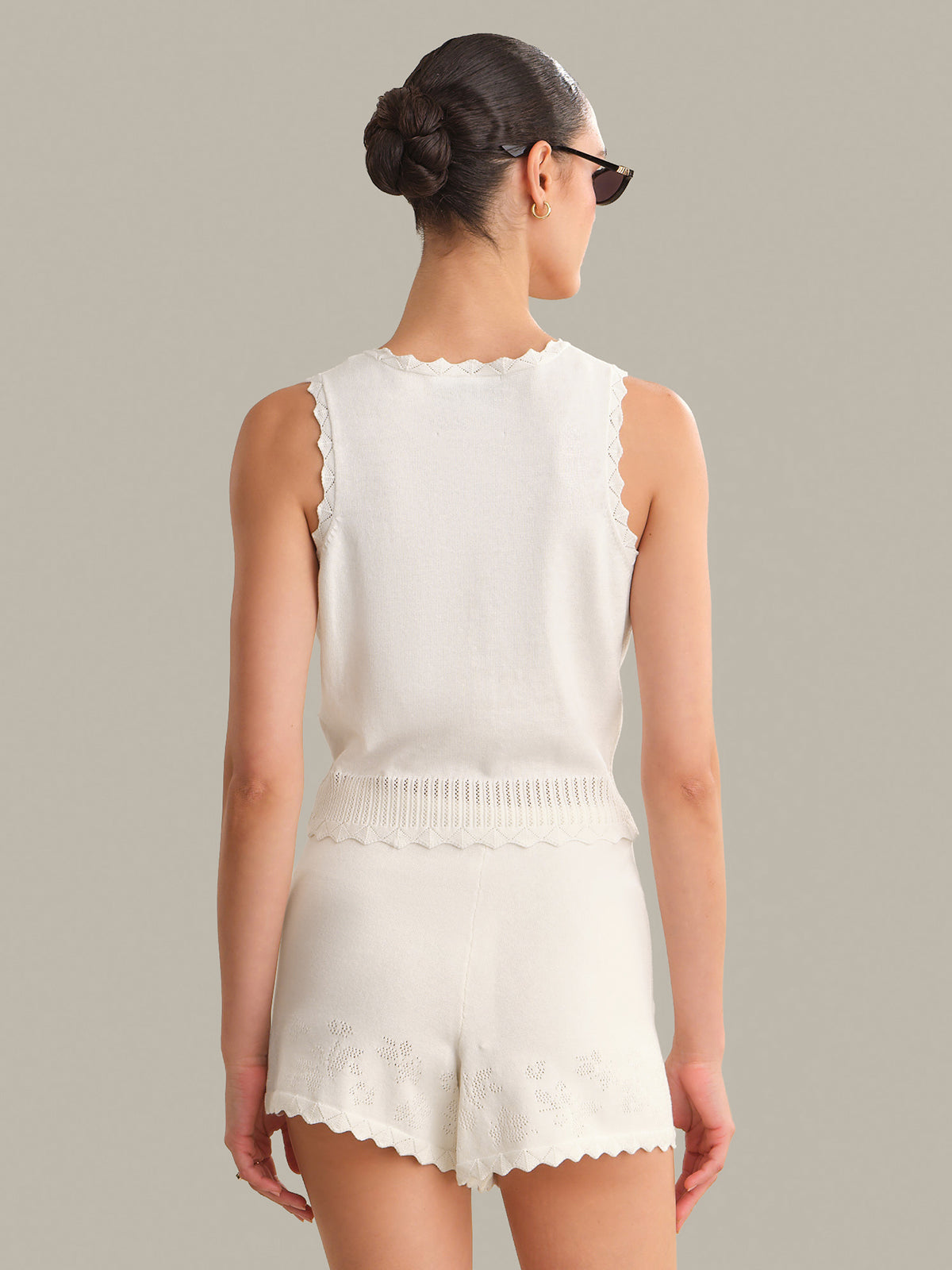 Woman wearing a white sleeveless top and shorts set on a neutral background