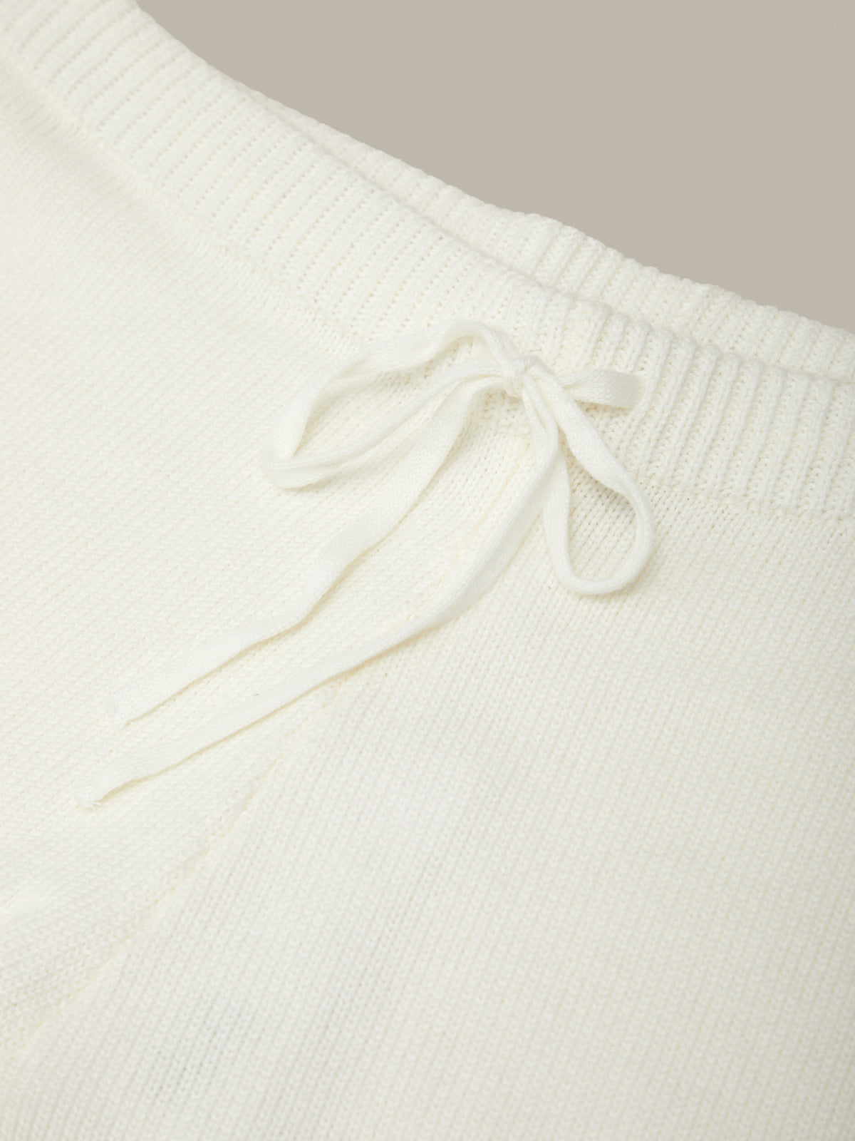 Close-up of a white knit sweater with a bow detail on a neutral background
