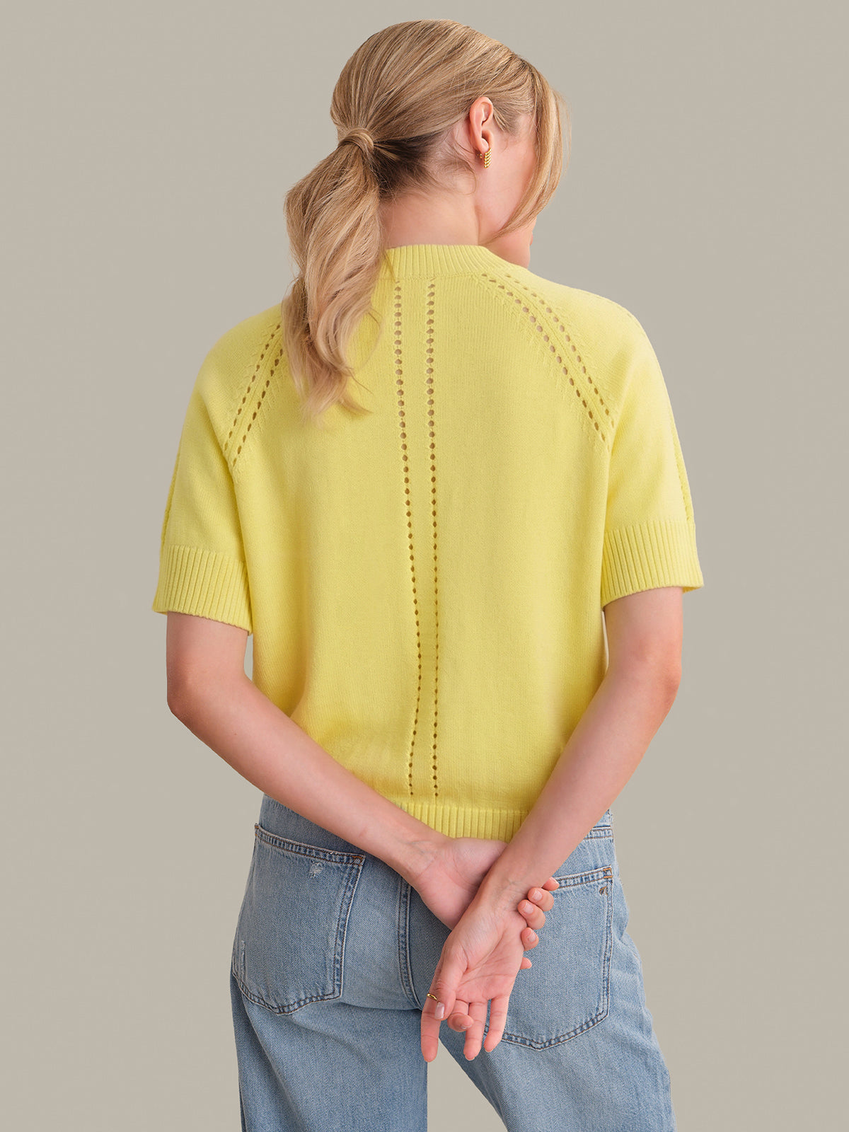 Person wearing a yellow knit top and blue jeans on a plain background