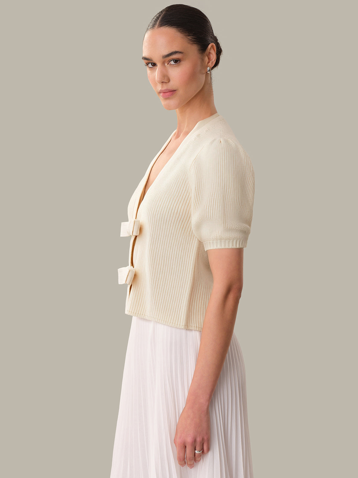 Woman wearing a cream-colored ribbed cardigan over a white dress on a neutral background
